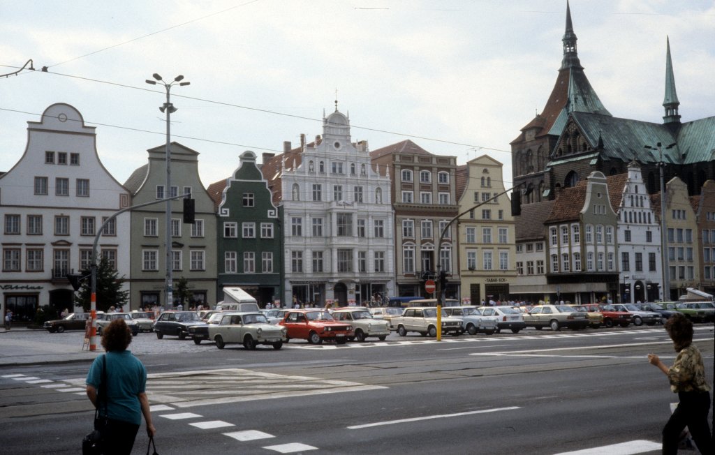 Rostock am 1. Juli 1990: Ernst-Thlmann-Platz. - In den Jahren 1952 - 1991 hiess Neuer Markt, der historische Markt der Rostocker Mittelstadt, 'Ernst-Thlmann-Platz'. Nach dem Zweiten Weltkrieg waren 90 Prozent der Huser hier zerstrt, die Giebelhuser an der Westseite des Marktes - die Huser auf dem Foto - wurden aber neu errichtet. Rechts ist ein Teil der Marienkirche zu sehen.
