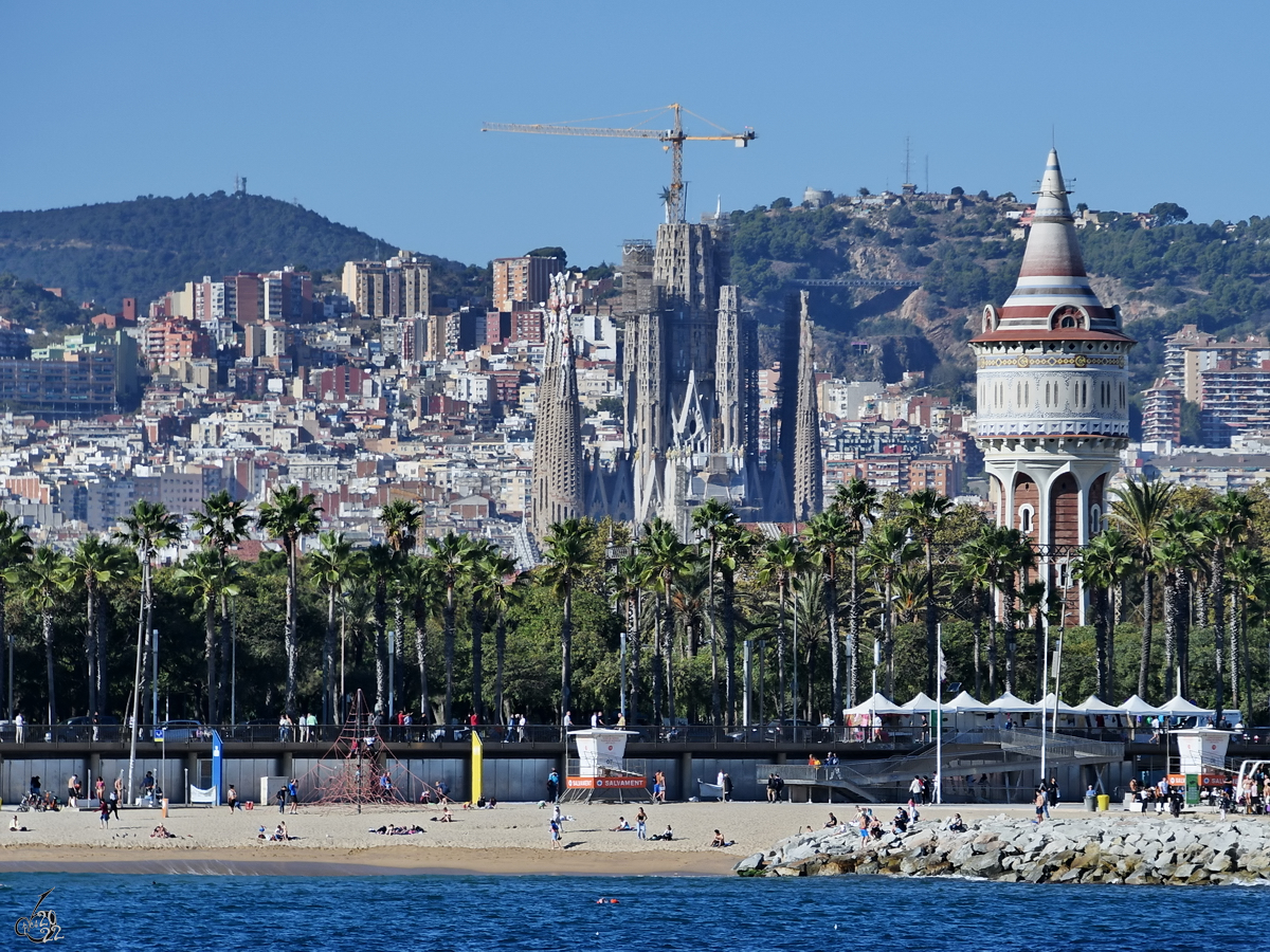 Blick vom Wasser auf den Strand von Barcelona, im Hintergrund deutlich zu erkennen der 45 Meter hohe Wasserturm  Torre d’aiges de la Catalana de Gas  und die  ewige Baustelle  Sagrada Famlia. (November 2022)

