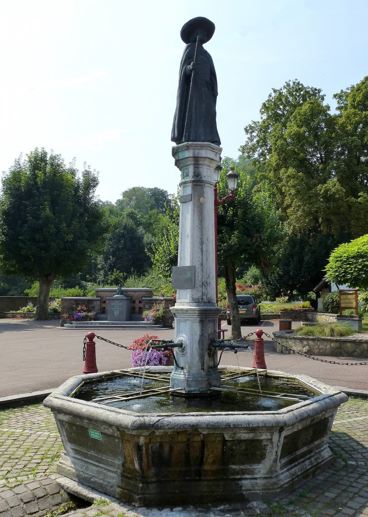 Blotzheim, der Brunnen am alten Rathaus von 1876, das Denkmal zeigt den berhmten Pfarrer des Ortes, Pere Bernadin Juif (1751-1836), Aug.2015