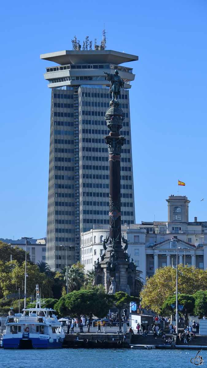 Das 1888 errichtete Kolumbus-Denkmal ist eine 60m hohe Sule mit Bronzestatue. Dahinter zu sehen das 1970 erbaute Hochhaus Coln, welcher mit einer Hhe von 100 Metern der erster Wolkenkratzer in Barcelona war. (November 2022)
