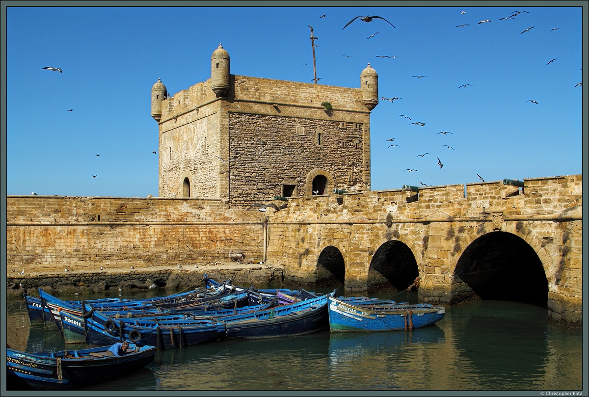 Die Scala du Port ist eine alte Festungsanlage aus der portugiesischen Besatzungszeit, welche den Hafen von Essaouira schtzte. Heute wird die Anlage als Museum und Aussichtspunkt genutzt. Vor dem Turm liegen einige der typischen blauen Fischerboote vor Anker. (Essaouira, 21.11.2015)