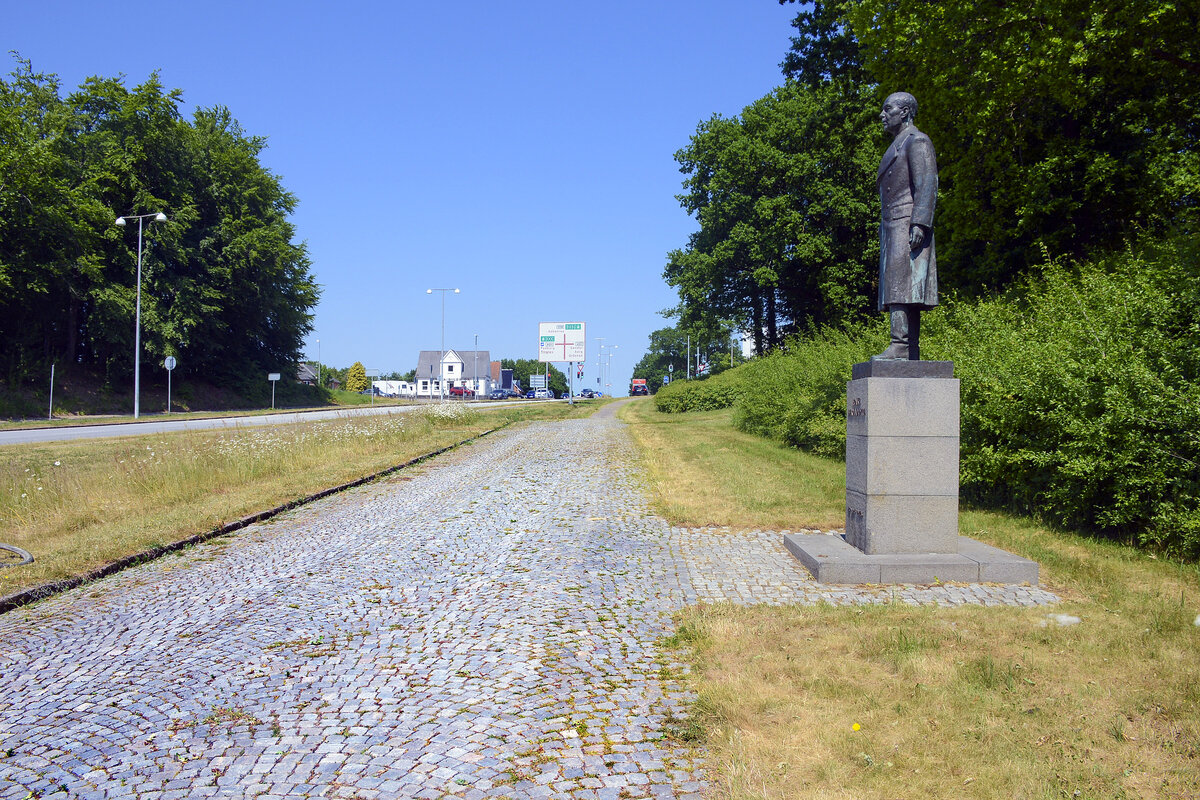 Ein erhaltener Abschnitt der alten Strae zwischen Flensburg und Apenrade. Auf der rechten Seite steht eine Statue des schwedischen Grafen Folke Bernadotte (18951948). Aufnahme: 11. Juni 2023.