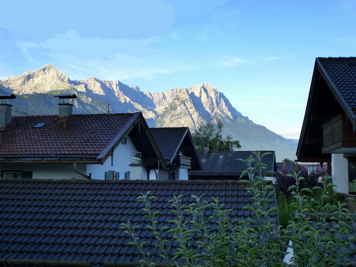 Garmisch-Partenkirchen, Blick am frhen Morgen ber die Dcher von Partenkirchen zum sonnenbeschienenen Zugspitzmassiv, Aug.2014