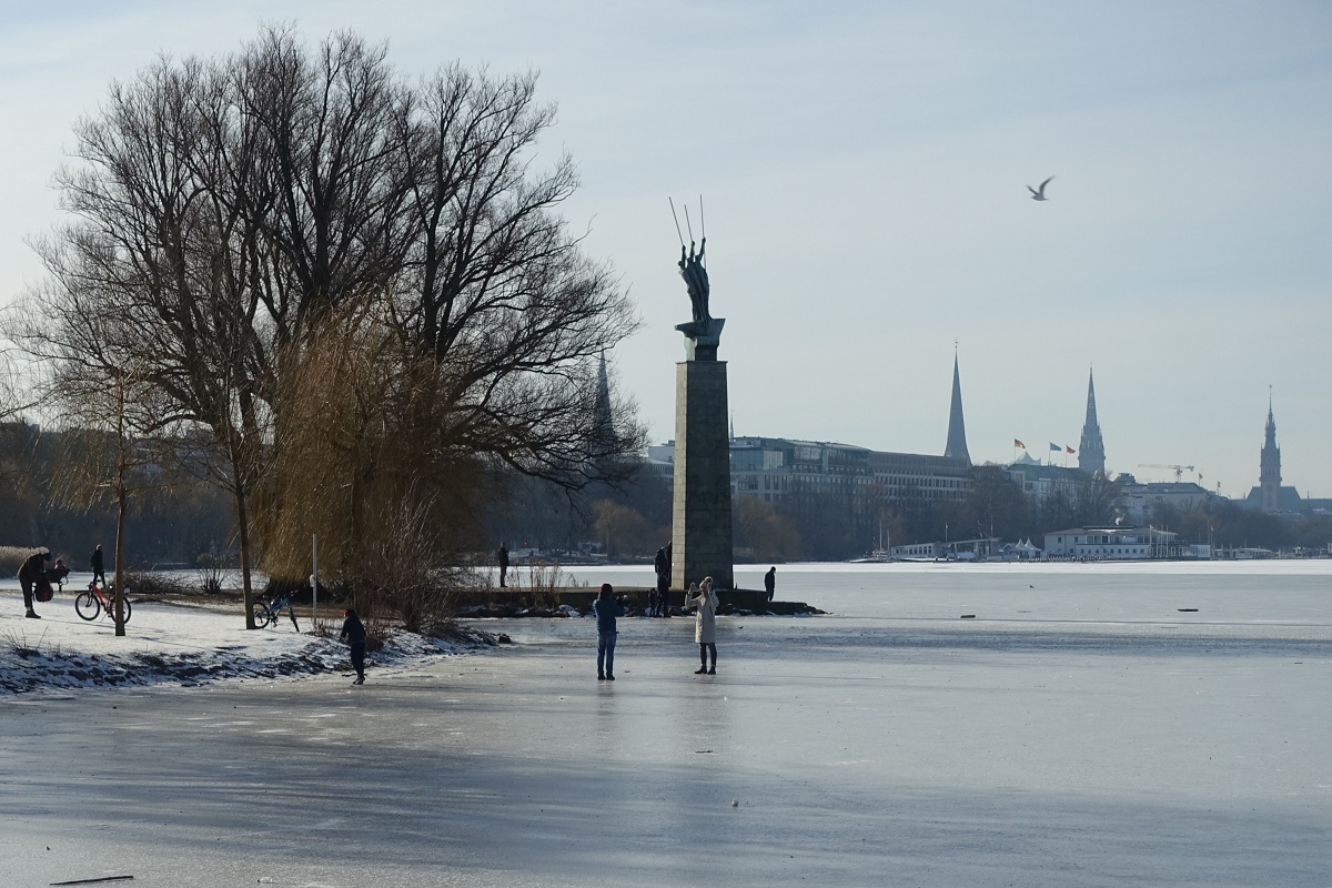 Hamburg-Hohenfelde am 14.2.2021: Blick auf die Alsterwiese Schwanenwik mit dem Denkmal „Drei Mnner im Boot“, weiterhin die sorglosen Mitbrger auf dem nicht freigegebenen Eis der Alster /