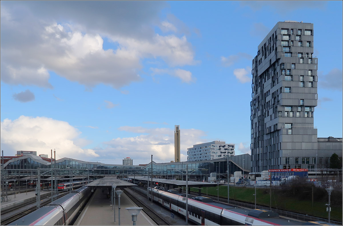 Moderne Architektur in Basel -

Blick von der Margarethenbrcke ber die Bahnsteige des Bahnhofes SBB. Rechts das 2019 fertiggestellte Meret Oppenheim Hochhaus der Basler Architekten Herzog & de Meuron. Links neben dem Hochhaus ist der hhere Bauteil des Komplexes Sdpark Baufeld D der ebenfalls von Herzog & de Meuron geplant wurde und 2012 fertig war.
ber die Gleise fhrt seit 2003 die 'Passerelle' von Cruz y Ortiz Arquitectos die sowohl dem Zugang zu den Bahnsteigen dient, als auch der Verbindung der Stadtquartiere nrdlich und sdliche des Bahnhofes.

08.03.2019 (M)