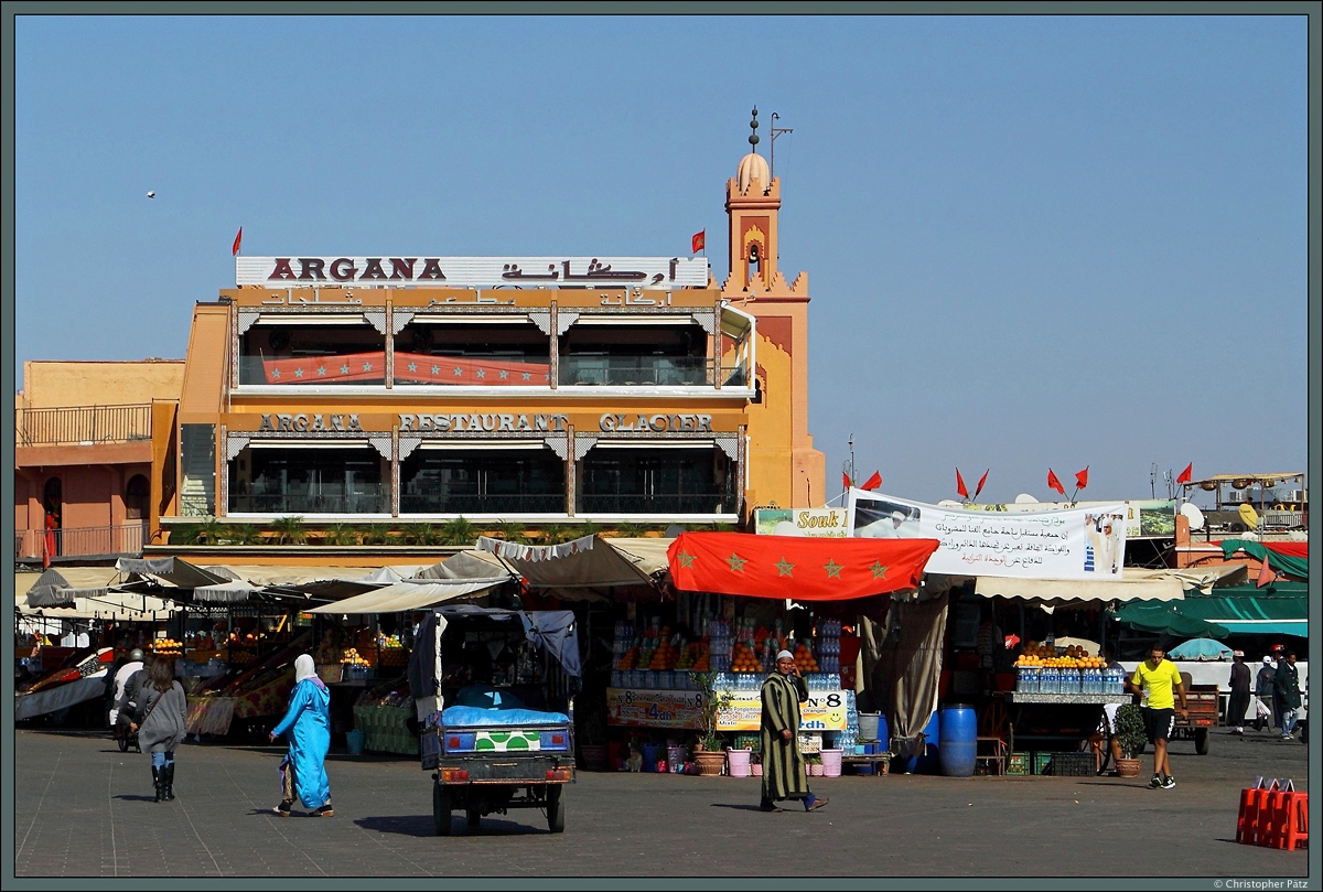 Tagsber wird der Platz Djama el-Fna im Zentrum Marrakeschs von Hndlern dominiert. Hier sind mehrere Stnde zu sehen, an denen beispielsweise frisch gepresster Orangensaft angeboten wird. Im Hintergrund ist das Minarett der Quessabine-Moschee zu sehen. (Marrakesch, 17.11.2015)