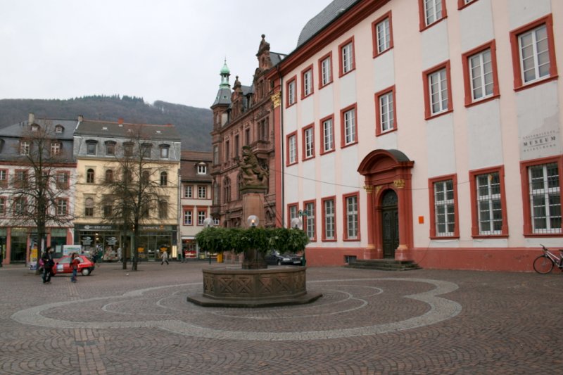 Universittsplatz Heidelberg. Rechts neben dem Brunnen sieht man den Eingang zur alten Uni, wo heute fast nur noch reprsentative Vreanstaltungen stattfinden. Die alte Aula wird z.B. als Raum fr Erstsemesterempfaenge benutzt oder fr Promotionsfeiern (ich durfte da auch schon mal rein ;) 