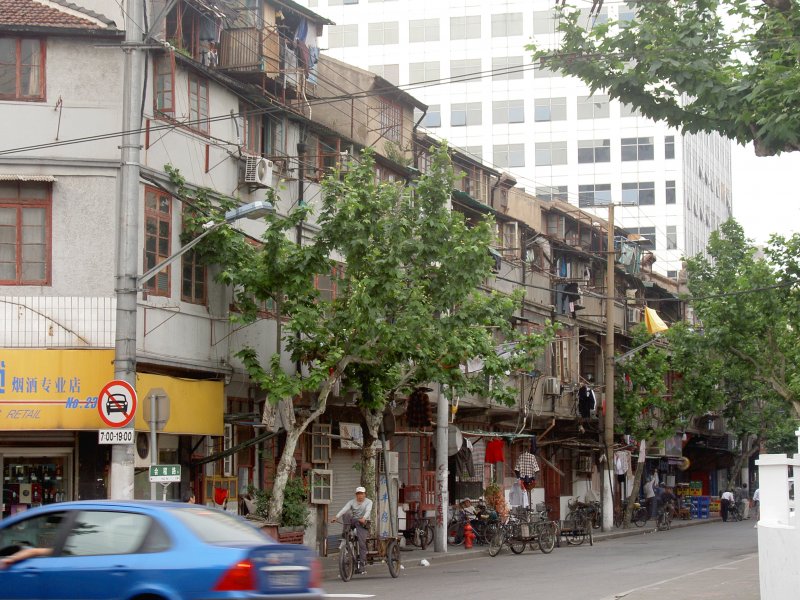 Wieder einmal eine ltere Wohnsiedlung zwischen den Hochhusern eingeklemmt.Shanghai Huji Lu (irgendwo in der Innestadt) 21.05.2005. Zu beachten ist auch, dass jeder eine Klimaanlage hat, die dort auch den ganzen Tag laufen muss, da die Fenster und Wnde misserabel isoliert sind.(Einfachverglasung und kein Kitt)