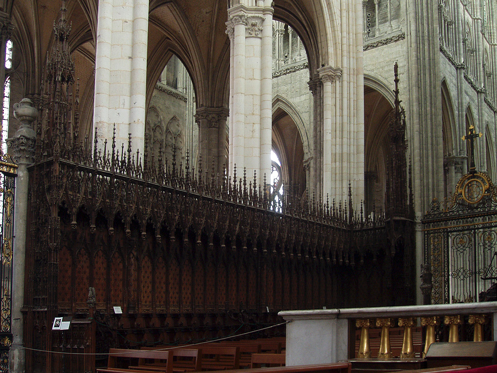 Amiens, Kathedrale Notre Dame. Die eine Hälfte des Chorgestühls, Südseite. Bemerkenswertes Beispiel gotischer Holzschnitzkunst. Links dahinter Blick in die beiden südlichen Chor-Seitenschiffe sowie Südquerhaus, rechts oben Teil der südlichen Langhauswand, rechts unten Teil des Lettners, barock. Aufnahme vom 24. Dez. 2003, 11:20