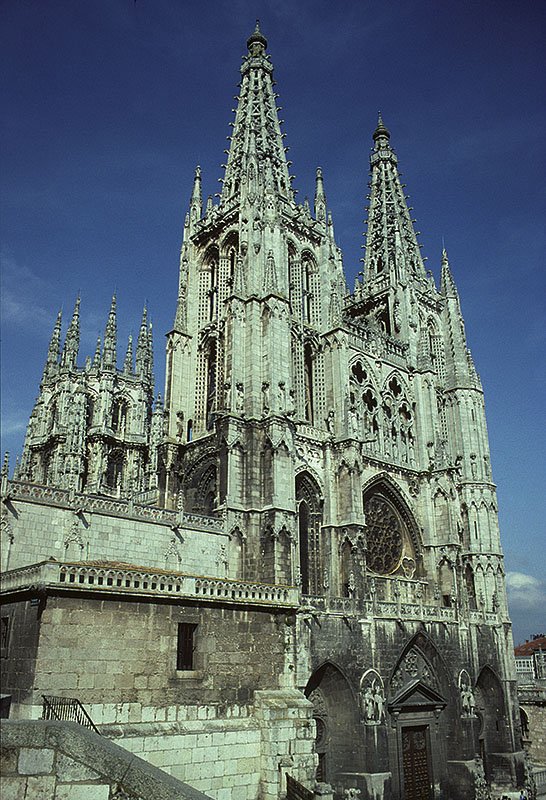 Burgos, Catedral Santa María, Bau ab 1221. Gotische Doppelturmfassade mit durchbrochenen Masswerk-Turmhelmen, 88 m hoch, wird Johann von Köln (Juan de Colonia) zugeschrieben, der mit Sicherheit auch den Fassadenplan  F  des Kölner Domes gekannt hatte. Links sichtbar die Laterne, die nach Einsturz des ersten Vierungsturmes auf verstärkten Pfeilern neu im Mudéjar-Stil aufgebaut wurde. Juni 1993, HQ-Scan ab Dia.