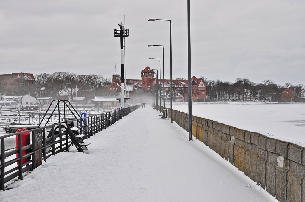 der Besucherstrom auf die Stralsunder Mole hlt sich in Grenzen - aber doch so einige haben sich den eisigen Wind um die Nase pfeifen lassen, was im Hintergrund das Bild etwas unscharf erscheinen lt - ist Flugschnee bei noch immer guten Windstrken, 09.01.2010