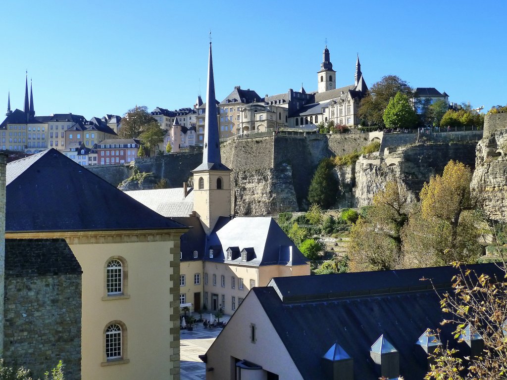 Luxemburg,vorne im Bild an der Alzette: die Abtei Neumnster und die Johanneskirche, auch St. Johann auf dem Stein genannt. Oben links: die Trme der Kathedrale (ursprnglich eine Jesuitenkirche, deren Grundstein 1613 gelegt wurde). Ende des 18. Jahrhunderts nahm die Kirche das Gnadenbild der Trsterin der Betrbten, der Stadt- und Landespatronin, auf. Oben rechts: die St.-Michaelskirche ist das lteste erhaltene sakrale Bauwerk der Stadt. Im Jahre 987 stand an der Stelle der heutigen St.-Michaelskirche die Burgkapelle der Luxemburger Grafen. Von links nach rechts auf dem Felsen, der Corniche Spazierweg, auch “der schnste Balkon Europas” genannt, verluft auf den von Spaniern und Franzosen im 17. Jahrhundert errichteten Wllen entlang des Alzette-Tales. Von der Rue de la Tour Jacob aus gesehen am 15.10.2011 