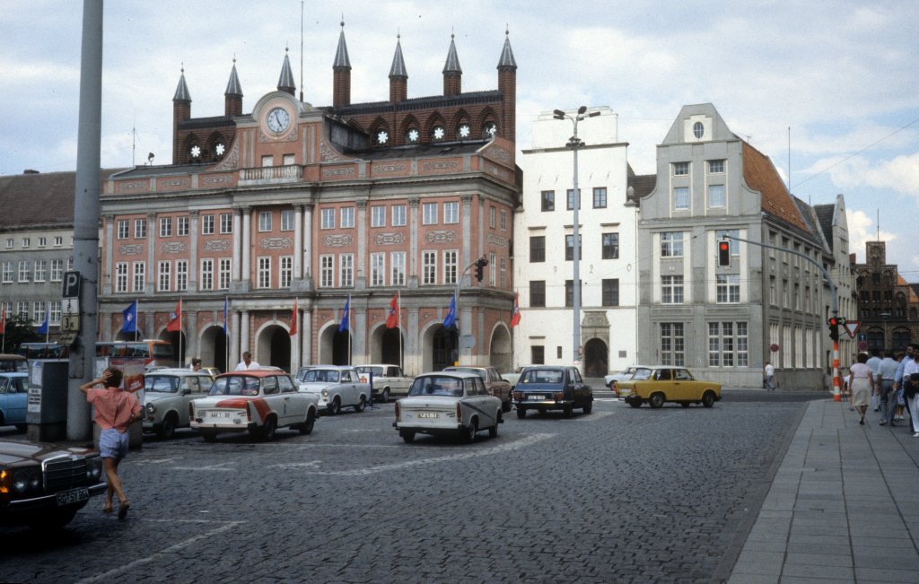 Rostock am 1. Juli 1990: Ernst-Thlmann-Platz, seit 1991 wieder Neuer Markt, mit dem Rathaus. Nur das oberste Teil des Rathausgebudes zeigt dem Betrachter, dass der ursprngliche Bau (aus dem 13. Jh) ein Backsteingebude war. Anstelle der Laube aus dem Mittelalter errichteten Zacharias Voigt und Joseph Petrini 1727 - 1729 einen dreigeschossigen Barockvorbau. - Ganz rechts ahnt man das Kerkhofhaus (An der Hege / Ecke Grosse Wasserstrasse), ein Backsteinhaus, das fr den Brgermeister Kerkhof um 1470 erbaut wurde.