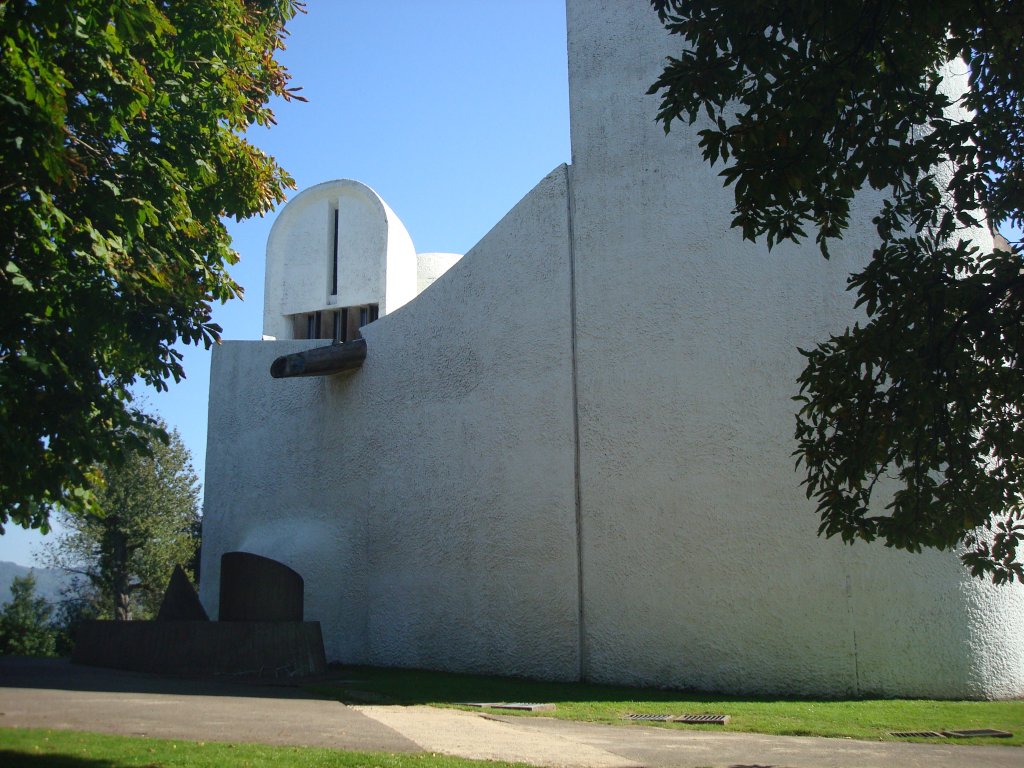 Wallfahrtskirche in Ronchamp / Frankreich, 
die fensterlose Westseite mit skulpturartigem Wasserspeier, dahinter der Nordturm und einer Brunnenskulptur vor der Wand,
Sept.2010