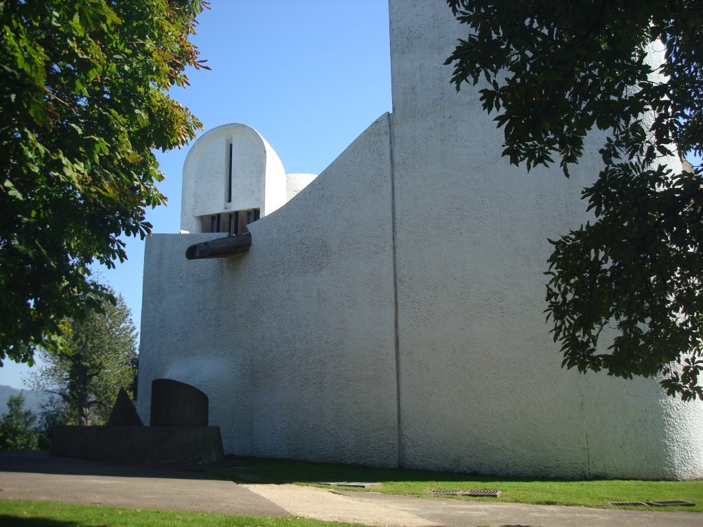 Wallfahrtskirche in Ronchamp / Frankreich, 
die fensterlose Westseite mit skulpturartigem Wasserspeier, dahinter der Nordturm und einer Brunnenskulptur vor der Wand,
Sept.2010