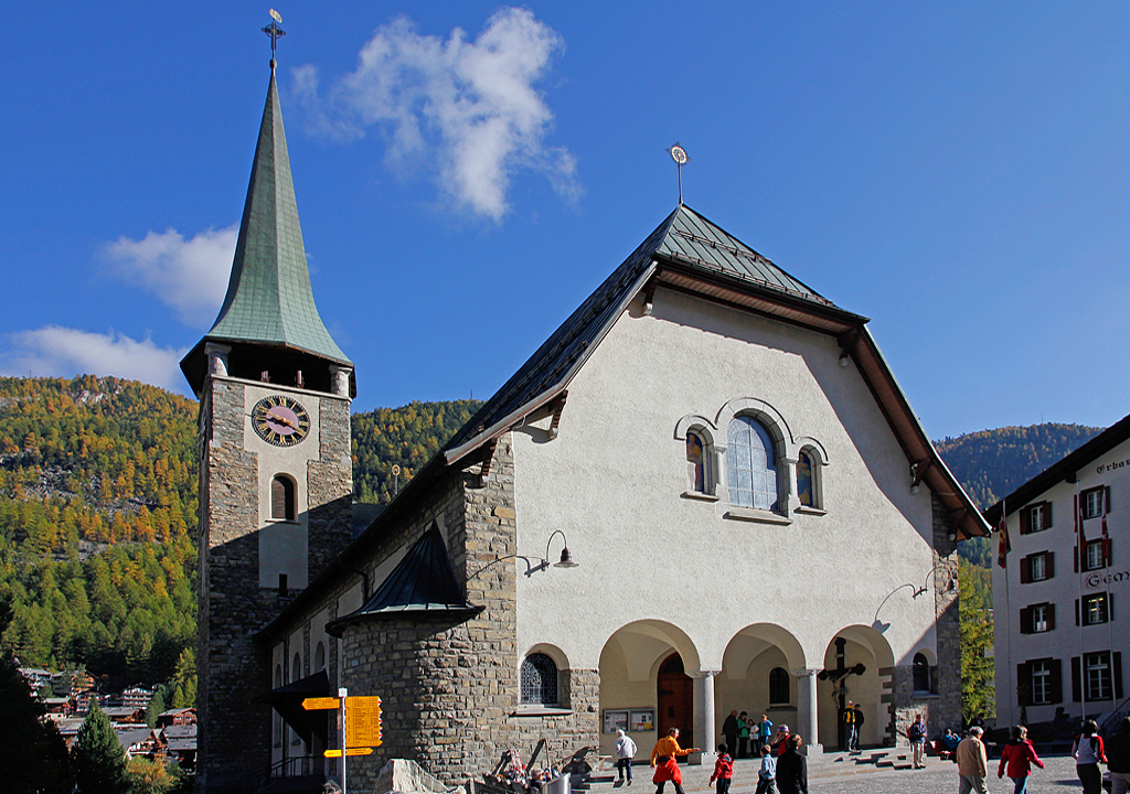 Zermatt, Pfarrkirche St. Mauritius. Westfassade mit abgewalmtem Dach und Rundbogen, links der flankierende Chorturm. 1910-1913 nach Plnen von Adolf Gaudy aus Rorschach realisierter Bau anstelle der kleineren, aus dem Mittelalter stammenden Vorgngerkirche. 1925 wurde die Turmuhr installiert, whrend die 3 neuen Glocken 1932 aufgezogen wurden. Aufnahme vom 13. Okt. 2011, 15:48
