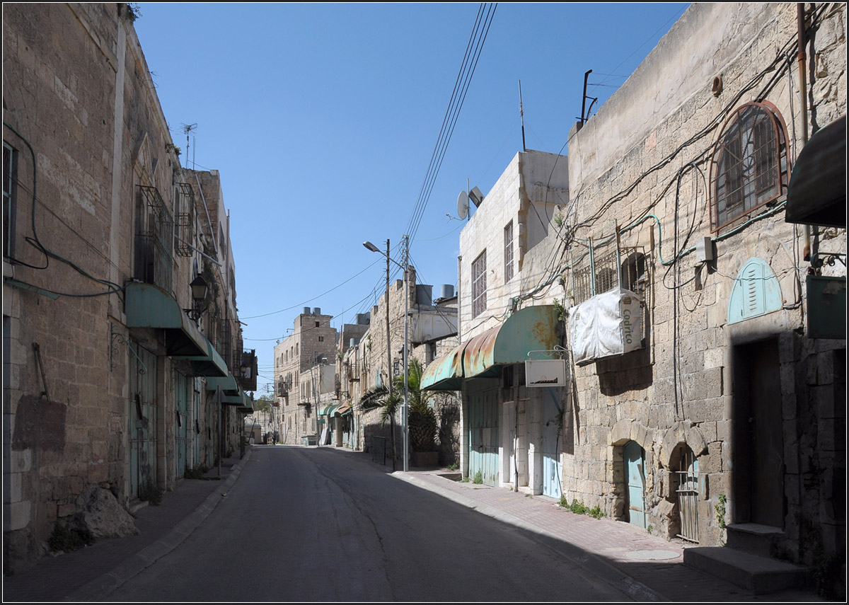 . Geisterstadt Hebron -

Blick in die nahezu tote David Ha'Melech Street. Um hier hin zu kommen muss man einen israelische Checkpoint passiern (im Hintergrund erkennbar). In dieser Strae wohnen noch Palstinenser, aber ihre Lden mussten geschlossen werden. Die Strae drfen sie nur zu Fu durchqueren. Weiter im Rcken von uns steht ein weitere Soldat. Ab da drfen die Palstinenser die Strae auch nicht mehr zu Fu betreten, da die Strae dann an Gebuden von jdischen Siedler vorbeifhrt. Die Spannungen zwischen Palstinensern und Juden sind in Hebron sehr gro, was zu diesen groen Einschrnkungen fr die Bewegungsfreiheit fr die Palstinenser fhrte und Hebron ber einen weiten Bereich zur Geisterstadt machte. Die jdischen Siedler haben sich hier mitten in der Innenstadt niedergelassen.

22.03.2014 (Jonas)