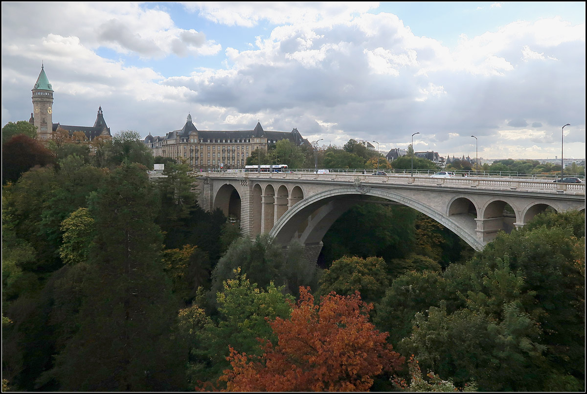 . Pont Adolphe in Luxemburg -

Die Adolphe Brcke fhrt ber das Tal der Ptrusse hinweg und ist einer von drei groen Straenviadukte, die die Innenstadt von Luxemburg ber die umgebenden Tler hinweg mit den angrenzenden Stadtteilen verbinden. Zwei dieser Brcken werden zuknftig auch von der Luxtram befahren werden. Von 2014 bis 2017 wurde die Pont Adolphe saniert und dabei auch Gleise fr die Straenbahn verlegt. Ersetzt man auf der Aufnahme gedanklich den Bus durch eine Tram, hat man das sptere Bild vor Augen, da die Straenbahn wie auch auf der Pont Grande-Duchesse Charlotte hier im Akkubetrieb ohne Oberleitungen betrieben werden.

Im Rahmen der Sanierung wurde unter die Straenfahrbahn der Pont Adolphe ein Steg zwischen die beiden Brckenhlften eingehngt, der vor allem fr Radfahrer aber auch fr Fugnger gedacht ist. Aus dieser Perspektive ist dieser Steg kaum wahrnehmbar.

03.10.2017 (M)