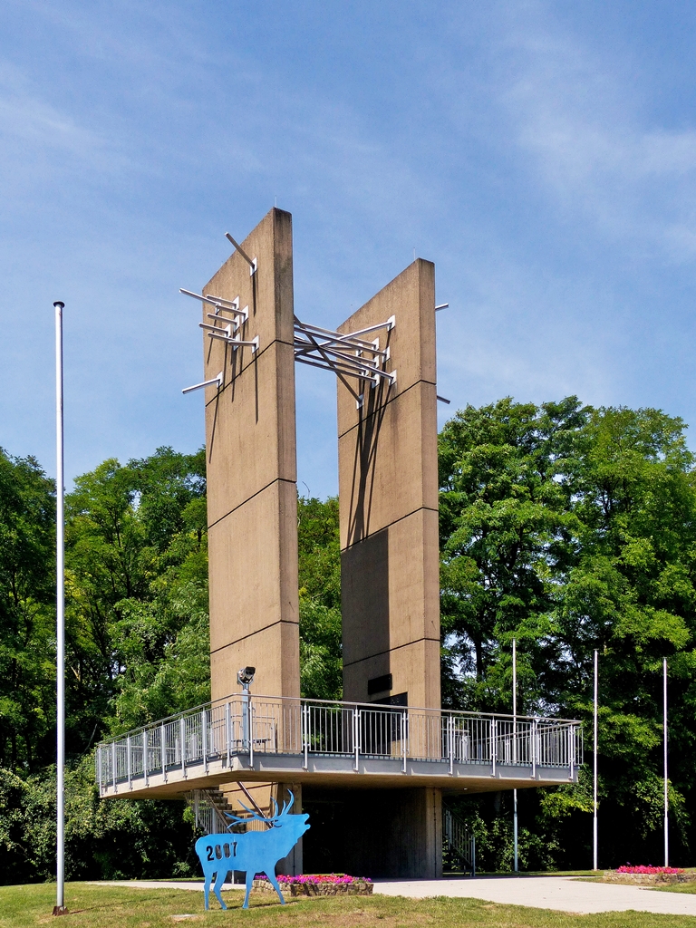 . Saarland - Das Europadenkmal in Berus in der Gemeinde berherrn. 18.07.2014 (Jeanny)

Das Europadenkmal besteht aus zwei senkrecht aufragenden, 16 m hohen Betonplatten, die in ihrem unteren Teil eine Aussichtsplattform mit durchsichtigem Gelnder durchbrechen. An ihren oberen Enden sind die beiden rechteckigen Pylone mittels eines Strahlenbndels aus mehreren Metallstben miteinander verbunden. Auf der Innenseite der beiden Pylone ist oberhalb der Plattform in Augenhhe eine Gedenktafel fr die Politiker Konrad Adenauer, Robert Schuman und Alcide De Gasperi angebracht. Weitere Plaketten fr Helmut Bulle, Josef Besch und Paul Henri Spaak wurden nach der Einweihung angebracht.

Das Europadenkmal ist heute das Wahrzeichen der Grenzgemeinde berherrn. Seine Lage und die Aussicht machen das Denkmal zum beliebten Haltepunkt auf Spaziergngen und Ausflgen. Die Stirnseite des Denkmals ist ungefhr in Richtung auf Saarbrcken orientiert, was auf die uralte Brckenfunktion des Saarraumes als Kreuzungspunkt von Fernwegen und auf seine weit jngere Brckenfunktion im deutsch-franzsischen Verhltnis verweist. Gerald Motsch versuchte, die deutsch-franzsische Geschichte im Laufe der Jahrhunderte in vertikaler Form durch die beiden Platten ins Bild zu setzen. Die horizontale Plattform des Denkmals signalisiert die gemeinsame historische Wurzel der beiden Nationalstaaten im keltisch, romanisch und germanisch geprgten frhgeschichtlichen Kulturraum. Whrend die Betonplatten auer im Untergrund und in der Plattform nirgends verbunden sind, wurde in ihrem oberen Teil durch die gebndelten Stbe eine Verbindung aus Metall, d.h. aus einem anderen Material geschaffen.

Der blaue Hirsch im Vordergrund erinnert an das Jahr 2007, als Luxemburg gemeinsam mit der Groregion europische Kulturhauptstadt war. Er diente als Logo dieses Ereignisses. 