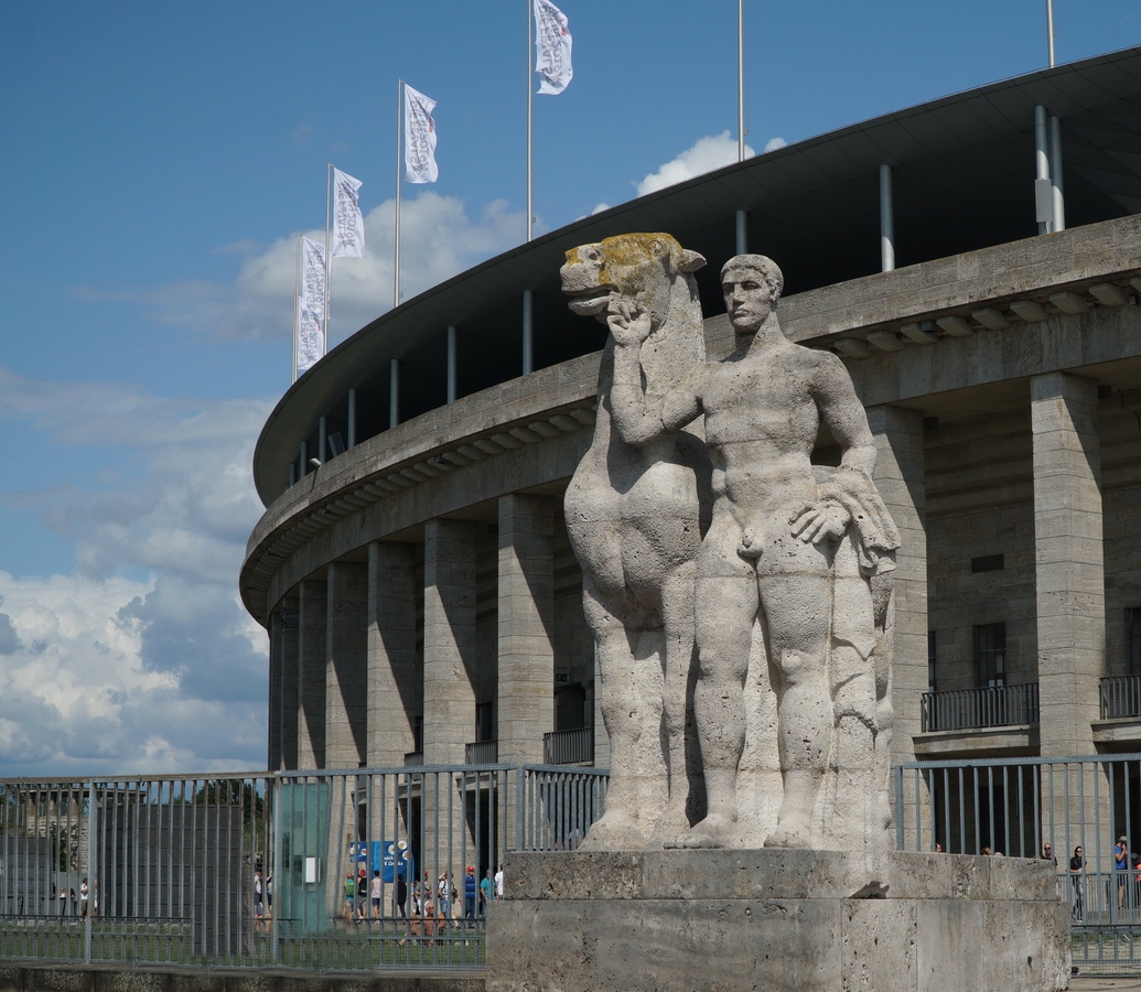 Am bergang vom Olympiastadion zum Maifeld stehen zwei Skulpturen  Rossefhrer  von Joseph Wackerle. Die Skulpturen aus Gauinger Travertin (Swasserkalkstein aus dem Landkreis Reutlingen in Baden-Wrttemberg) wurden vor Ort vom Knstler aus einem groen Steinquader herausgearbeitet. Foto: Sommer, 2019