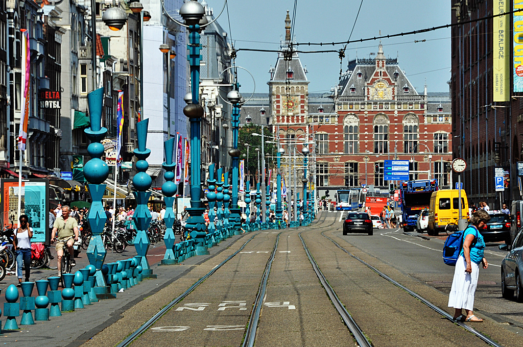 Amsterdam -  Damrak , Geschftsstrae und im Hintergrund der Bahnhof. Die Dame rechts unten im Bild hat Ihr T-Shirt farblich passend zu den  Skulpturen  am linken Strassenrand angepat - 23.07.2013