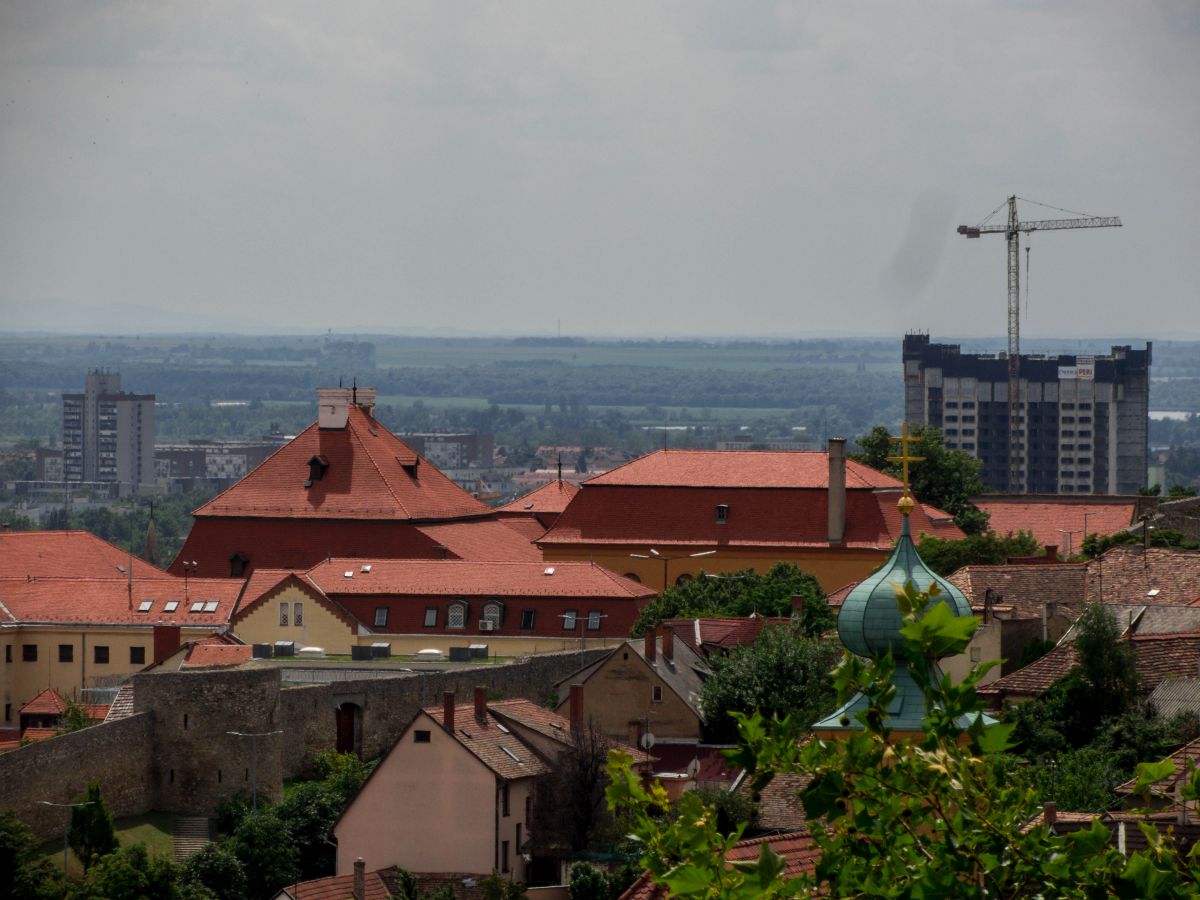 Auf de rechten seite ist das (ehemalig) 25 stckige Hochhaus zu sehen. Wegen verrostung ist das Gebude seit Jahrzenten nicht bewohnbar. Damit war es das hchste unbewohnte Haus von Zentraleuropa. Der Abriss war ursprnglich fr 2014 geplant, erst aber 2016 realisiert. Auf der linken Seite siet man das 17 stckige Haus, das aktuell hchste (Wohn)Gebude von Pcs. Unten links luft der Mauer, der auch die Grnze der historischen Altstadt bedutet. Stand: Mai 2016