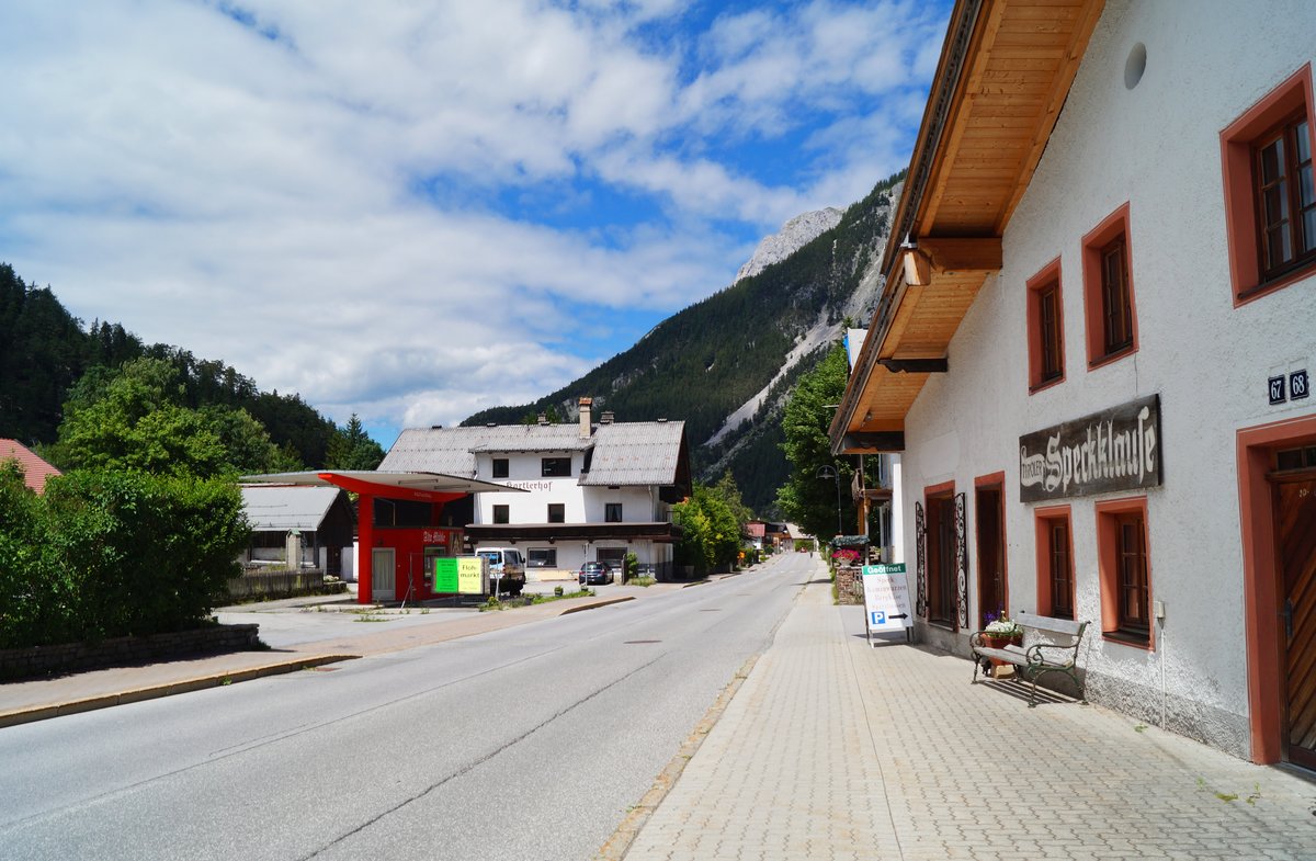 Auf der Innsbruckerstrae im Tiroler Grenzort Scharnitz. Blick in Richtung Mittenwald/Deutschland, zur Rechten befindet sich die  Tiroler Speckklause , eine Metzgerei mit typischen lokalen Produkten im Angebot. Aufnahme vom heien 5. Juli 2020. Zur Zeit der Aufnahme war die Durchgangsstrae trotz des hohen Reiseverkehrs glcklicherweise fast ganz leer... 