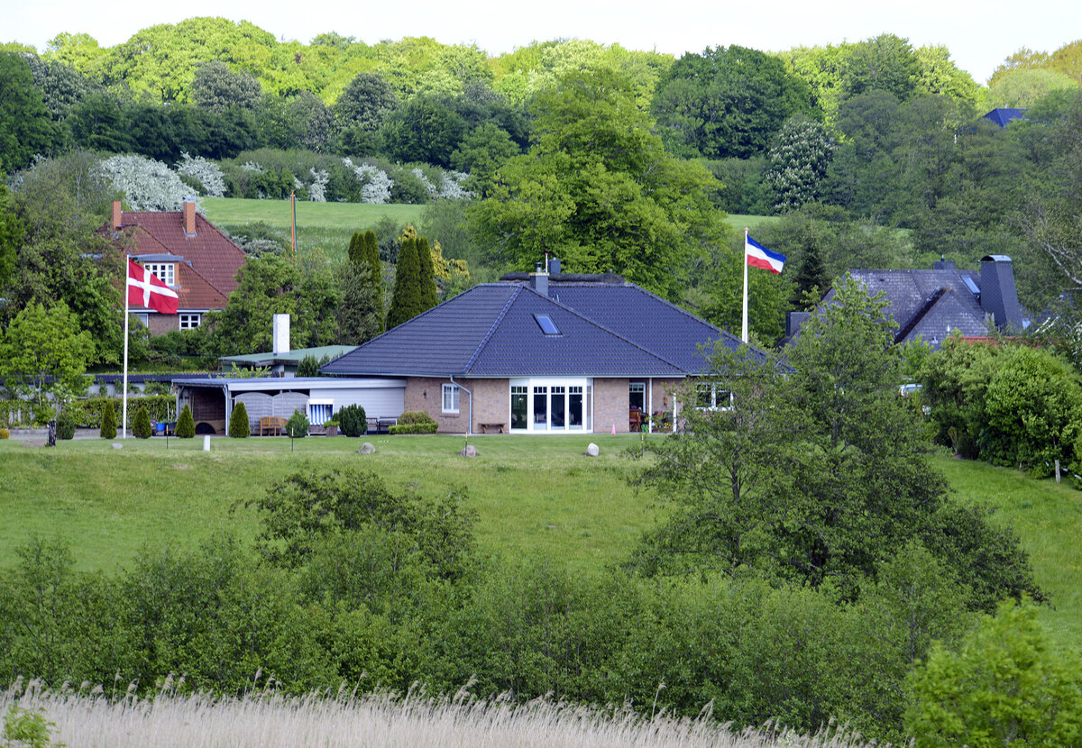 Blick auf einen Teil des Dorfes Niehuus in der Gemeinde Harrislee. Auf dem einen Grundstck weht die Dannebrog-Flagge, auf dem anderen die Schleswig-Holstein-Flagge. Aufnahme: 28. Mai 2023.