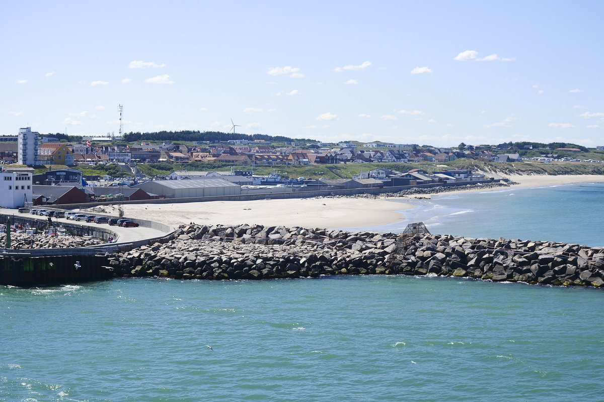 Blick auf Hirtshals von der Norwegen-Fhre. Der Hirtshalser Hafen hat aber auch Bedeutung als Verkehrshafen, unter anderem bestehen Fhrverbindungen nach Norwegen (Color Line und Fjord Line) sowie zu den Frer-Inseln und nach Island mit der Smyril Line. Die Verbindung Hirtshals - Kristiansand zhlt zu den wichtigsten Fhrverbindungen zur Skandinavischen Halbinsel.
Aufnahme: 1. Juli 2018.