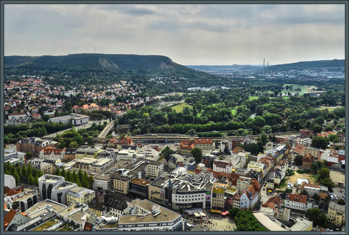 Blick vom Jentower Richtung Sden: Direkt neben der Saale, die sich durch die Stadt schlngelt, befindet sich der Bahnhof Jena-Paradies. Auf der anderen Seite des Flusses liegt der Seidelpark. Im Hintergrund ist das Heizkraftwerk Jena mit den zwei markanten Schornsteinen zu erkennen. Der 1981 errichtete, 225 m hohe Schornstein ist das hchste Bauwerk in Thringen. Neben dem Kraftwerk befinden sich dies Stadtteile Lobeda (links) und Winzerla (rechts). Links auf dem Berg ist der Funkturm Kernberge zu erkennen. (Jena, 01.09.2016)