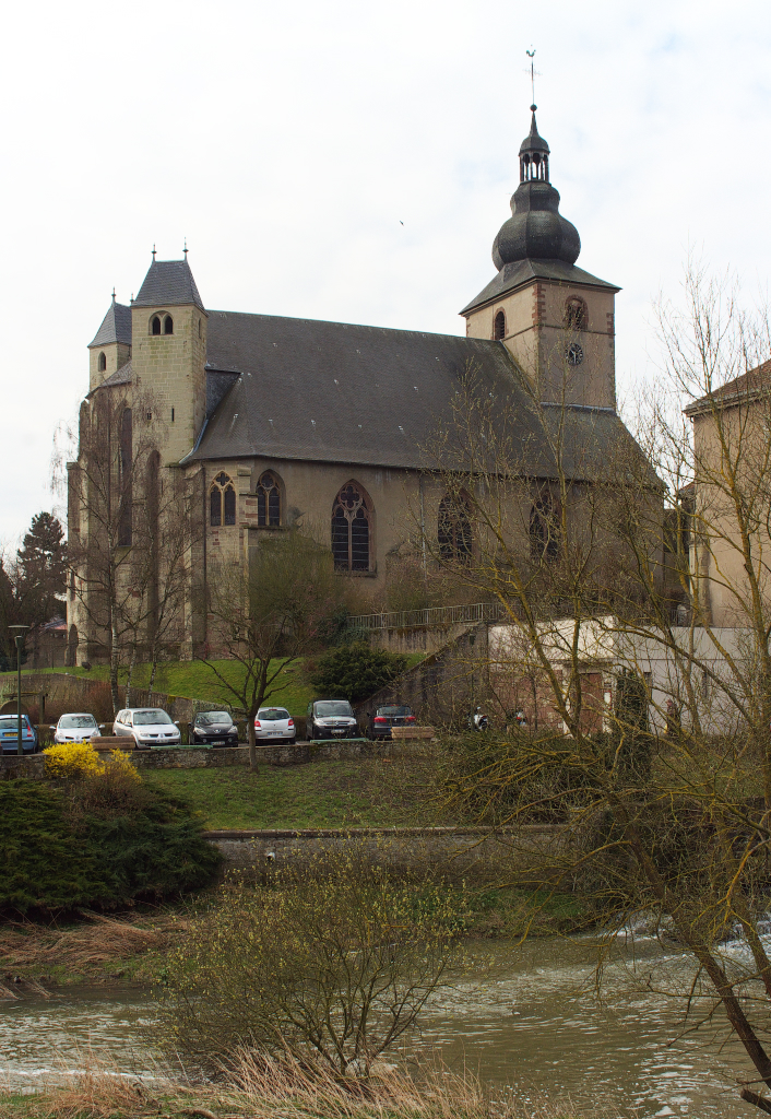 Blick ber das Fsschen Nied zur Kirche Sainte Croix (ehemalige Klosterkirche)in Bouzonville - Die Kirche ist eine ohne Querschiff erbaute gotische Pseudo-Basilika mit offener Vorhalle. Der Turm erhielt in der Barockzeit eine welsche Haube. Das Chorgesthl mit figrlichen Schnitzereien entstammt der Barockzeit. Der Chorabschluss der Kirche verfgt ber zwei fr Lothringen typische Chorflankentrme. Das Mittelschiff ist 17 m hoch, die Seitenschiffe erreichen eine Hhe von 10 m. 03.04.2015