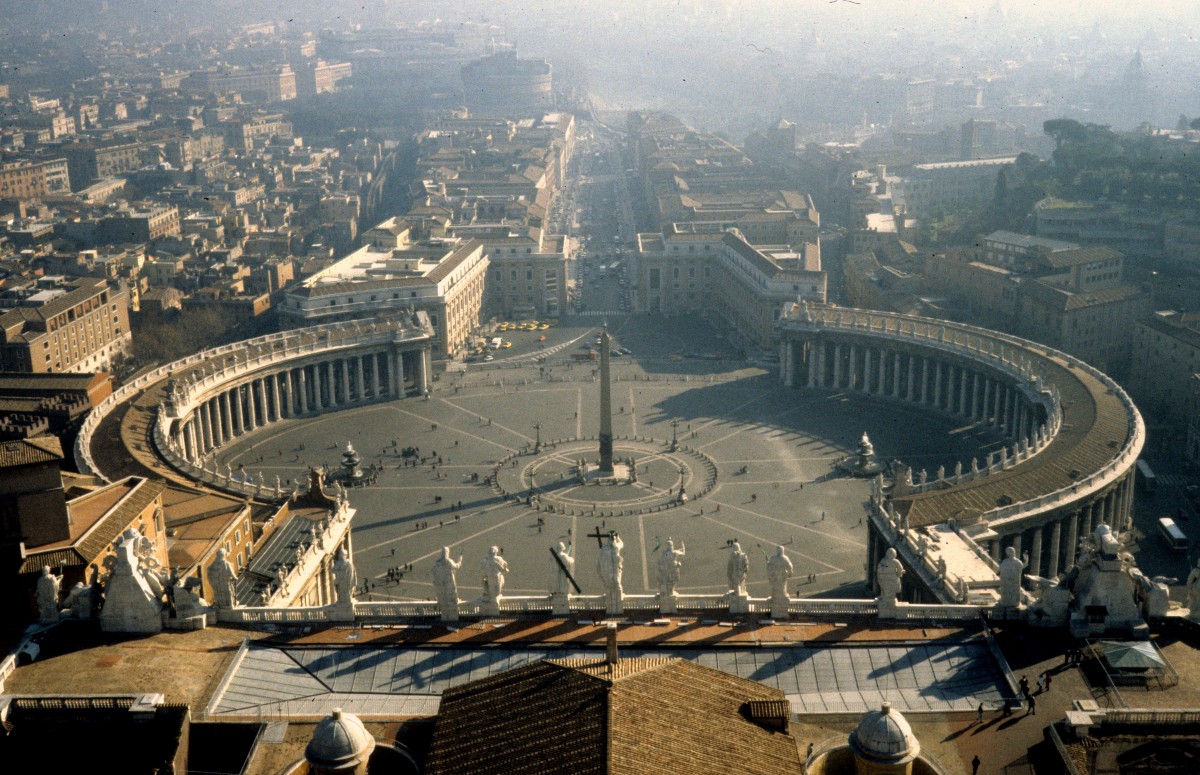 Citt del Vaticano / Vatikan - Roma / Rom im Februar 1989: Blick vom Petersdom auf die Piazza San Pietro / den Petersplatz und die Via della Conciliazione. Die Strasse wurde in den Jahren 1936 bis 1950 im Zuge der Lateranvertrge vom Jahre 1929 angelegt. In Verbindung mit der Anlage der Strasse und der Errichtung der neuen Huser wurden 600.000 m2 Gebude, darunter mehrere Kirchen und andere historische Gebude, entfernt, so dass dieser Stadtteil, il Borgo (aus dem Althochdeutschen 'burg'), einen grossen Teil seines historischen Charakters einbsste. - Im Hintergrund ahnt man die Engelsburg und den Tiber.