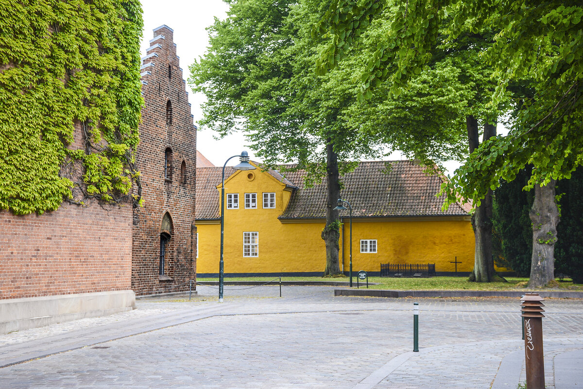 Das Backsteingebude auf der linken Seite ist Teil des Dom zu Roskilde. Das gelbe Gebude auf der rechten Seite ist Teil des Museums fr zeitgenssische Kunst (dnisch Museet for Samtidskunst) in Roskilde.Aufnahme: 20. Juni 2023.