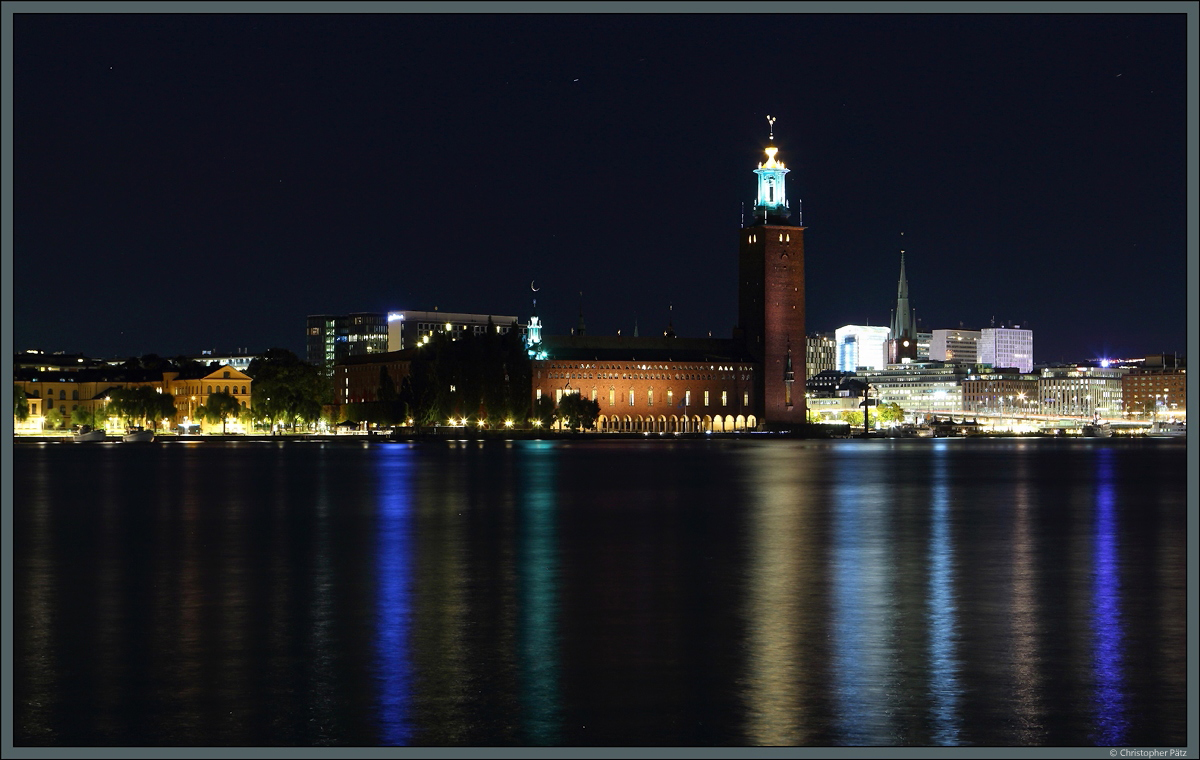 Das zwischen 1911 und 1923 erbaute Rathaus von Stockholm (Stockholms stadshus) liegt auf der Insel Kungsholmen. Am 26.09.2021 spiegeln sich die Lichter des Stadtzentrums im Wasser.