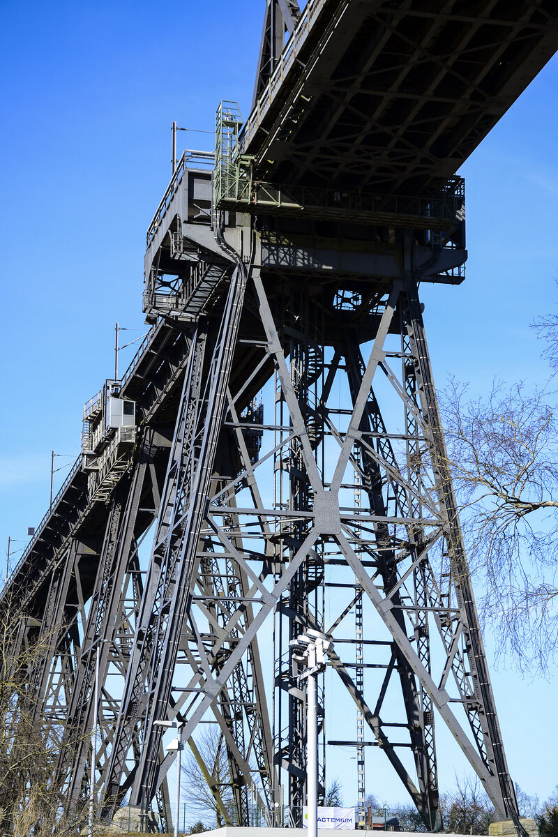 Detailaufnahme der Rendsburger Hochbrcke. Die Brcke berspannt den Nord-Ostsee-Kanal und dient als Eisenbahnbrcke, auerdem trgt sie eine angehngte Schwebefhre fr den Fugnger- und Fahrzeugverkehr. Sie ist Wahrzeichen der Stadt Rendsburg und eines der bedeutenden Technikdenkmler in Deutschland. 2013 wurde sie von der Bundesingenieurkammer als Historisches Wahrzeichen der Ingenieurbaukunst in Deutschland ausgezeichnet  Direkt unter der Brcke befindet sich die Schiffsbegrungsanlage Rendsburg. Aufnahme: 7. Mrz 2022.