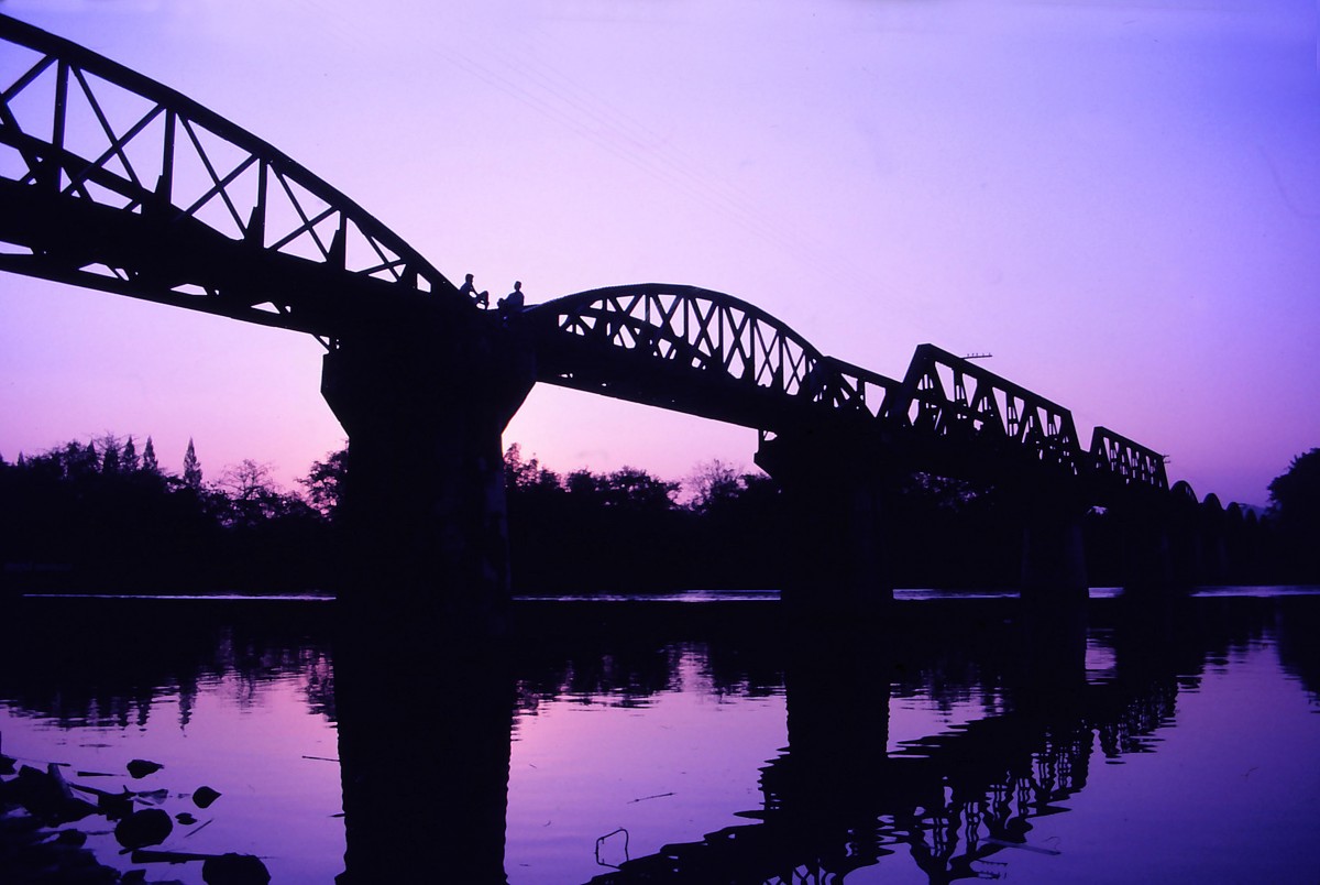 Die Brcke ber den Kwai in Kanchanaburi im Westen der Zentralregion von Thailand. Sie ist eine Eisenbahnbrcke im Zuge der Thailand-Burma-Eisenbahn. Abendaufnahme von Februar 1989 (Bild vom Dia).