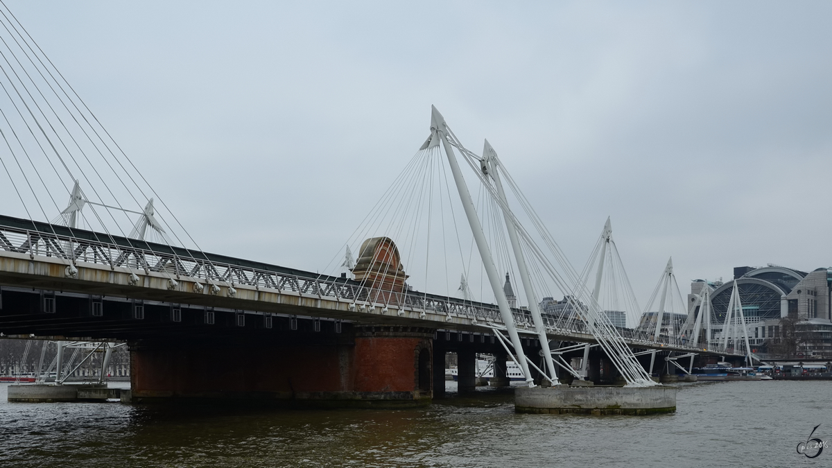 Die Eisenbahnbrücke  Hungerford Bridge   bildet die Hauptzufahrt zum Kopfbahnhof Charing Cross. Sie wird auf beiden Seiten von Fußgängerbrücken, den  Golden Jubilee Bridges  flankiert. (London, März 2013)