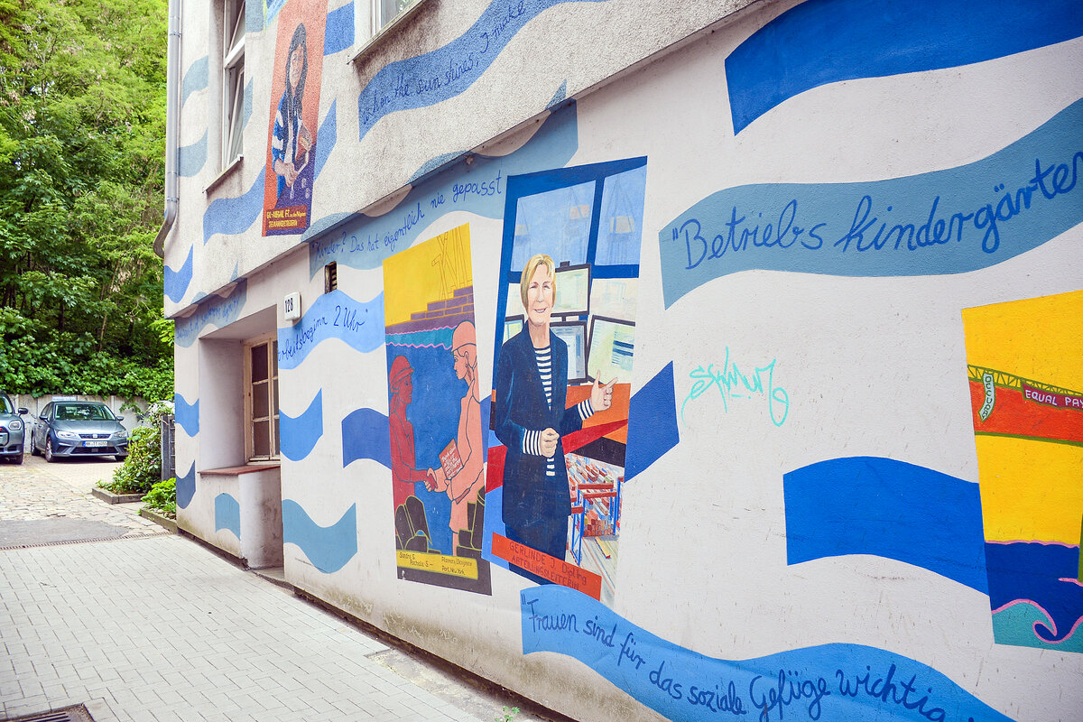 Die FrauenFreiluftGalerie in Altona ist eine einzigartige Open-Air-Galerie am Elbufer in Hamburg. Seit 1994 erz�hlen gro�formatige Wandbilder die Geschichte der Frauenarbeit im Hafen – von Fischverarbeitung bis Handel und Industrie. Internationale K�nstlerinnen machen den Wandel weiblicher Arbeitswelten sichtbar. Die rund zwei Kilometer lange Galerie ist kostenlos, barrierefrei und rund um die Uhr zug�nglich.
Aufnahme: 19. Mai 2026.