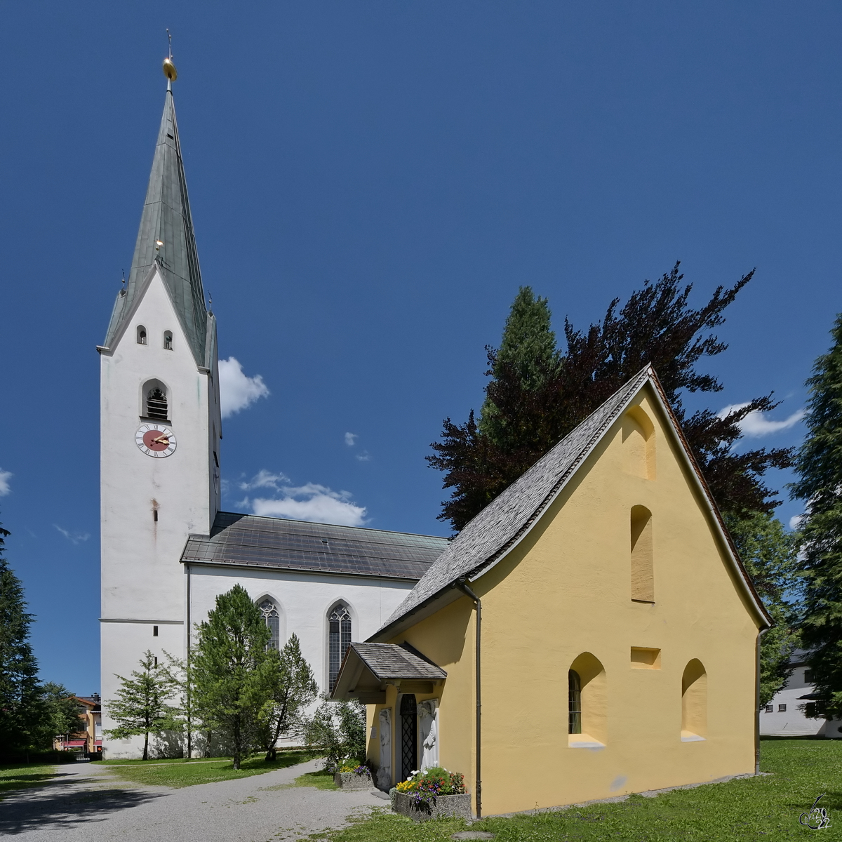 Die katholische Pfarrei St. Johannes Baptist wurde 1872 im neugotischen Stil wiederaufgebaut, nachdem die vorherige Kirche im Jahre 1865 durch einen Brand grtenteils zerstrt worden war. Das Gebude im Vordergrund ist die Seelenkapelle. (Oberstdorf, AJuli 2017)