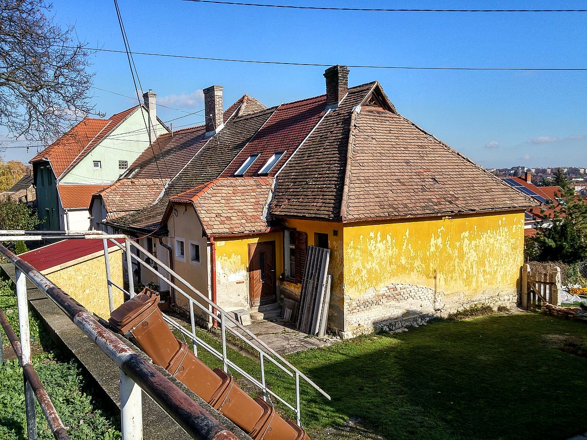 Dieses Foto habe ich in Pcs, in der Stadtteil  Erzsbettelep  (Elisabethsiedlung) gemacht. Dieser Stadteil wurde durch die Donaudampfschiffgesellschaft gegrndet. Die  Kolonie  stand aus 4 Strassen und 32 Huser. Es gab 6 kleine Wohnungen pro Haus zzgl Gartenteil und Nebengebude. Vor ca. 100-120 Jahren wurden neue Kohlenminien in der Nhe erffnet und die dort arbeitenden haben hier Wohnungen bekommen. Die Siedlung hie ursprnglich Ullmannsiedlung, genannt nach einem Leiter des Unternehmens. 1938 wurde auf Elisabethsiedlung umbenannt (von Elisabeth Amalie Eugenie von Wittelsbach Knigin genannt). Die Huser waren berdurchschnittlich ausgerstet, da Leitungswasser und Strom auch vorhanden war. In den vergangenen guten Jahrhundert wurde es nicht geregelt wie man die Gebuden/Wohnungen ndern, erweitern, umbauen oder zusammenlegen/vereinigen darf. Deswegen ist auf heutzutage das Strassenbild ganz ganz gemischt (und daher meiner Meinung nach, sehr einzigartig und interessant) geworden. Die Etagen wurden gendert, Dachgeschosse wurden eingebaut...daher findet man hier keine zwei gleiche Huser. Die groe nderungen sind um ca 1926 begonnen. Wegen der damaligen Wohnungsmangel hat die Stadt 2/3-tel der Siedlung in Miete genommen und hat unter anderem eine Kirche und Schule erbaut und geffnet. Aufnahmezeit: November 2020.
Der Gebudeteil vorne ist vermutlich durch ltere Leute bewohnt die kein Geld und/oder keine Nerven fr eine Sanierung haben.
Hier gilt es auch: 1 Dachfliesentyp = 1 Hausteil = 1 Eigentmer