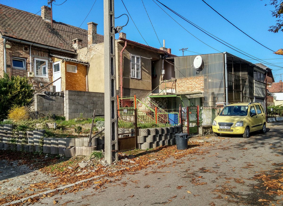 Dieses Foto habe ich in Pcs, in der Stadtteil  Erzsbettelep  (Elisabethsiedlung) gemacht. Dieser Stadteil wurde durch die Donaudampfschiffgesellschaft gegrndet. Die  Kolonie  stand aus 4 Strassen und 32 Huser. Es gab 6 kleine Wohnungen pro Haus zzgl Gartenteil und Nebengebude. Vor ca. 100-120 Jahren wurden neue Kohlenminien in der Nhe erffnet und die dort arbeitenden haben hier Wohnungen bekommen. Die Siedlung hie ursprnglich Ullmannsiedlung, genannt nach einem Leiter des Unternehmens. 1938 wurde auf Elisabethsiedlung umbenannt (von Elisabeth Amalie Eugenie von Wittelsbach Knigin genannt). Die Huser waren berdurchschnittlich ausgerstet, da Leitungswasser und Strom auch vorhanden war. In den vergangenen guten Jahrhundert wurde es nicht geregelt wie man die Gebuden/Wohnungen ndern, erweitern, umbauen oder zusammenlegen/vereinigen darf. Deswegen ist auf heutzutage das Strassenbild ganz ganz gemischt (und daher meiner Meinung nach, sehr einzigartig und interessant) geworden. Die Etagen wurden gendert, Dachgeschosse wurden eingebaut...daher findet man hier keine zwei gleiche Huser. Die groe nderungen sind um ca 1926 begonnen. Wegen der damaligen Wohnungsmangel hat die Stadt 2/3-tel der Siedlung in Miete genommen und hat unter anderem eine Kirche und Schule erbaut und geffnet. Aufnahmezeit: November 2020.
Das hier abgebildete Haus wurde ursprnglich anscheinend auf ca 4 Einheiten verteilt und in die Einheiten wurden nachtrglich mehr oder weinger erweitert (s. Etagen und Gre der Vorgarten).