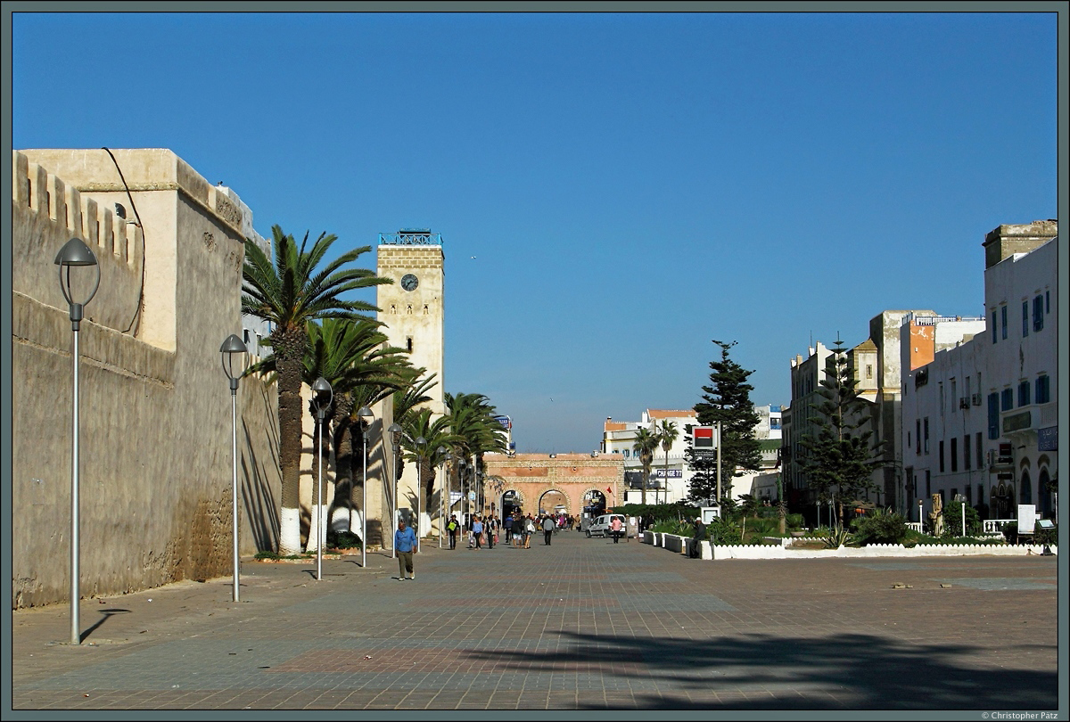 Eine Besonderheit der Medina von Essaouira ist das rechtwinklige Straennetz. Eine der Hauptstraen ist die Avenue Oqba Ibn Nafiaa, die auch das Stadttor Bab Moulay Youssef im Hintergrund durchquert. Links ist ein Teil der Stadtmauer zu sehen. (Essaouira, 21.11.2015)
