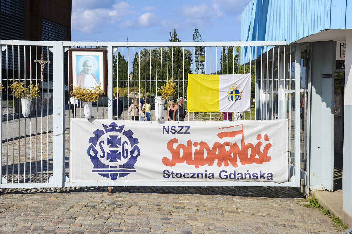 Eingang zur Werft Danzig AG. Die Werft ist Nachfolger der bis 1990 in Danzig (Gdańsk) bestehenden Leninwerft. Die Arbeiter der Werft galten seit den 1960er Jahren als aufmpfig und eigensinnig. Im Dezember 1970 wurden (illegale) Streiks und Arbeitsniederlegungen durchgefhrt, die von der Staatsmacht blutig niedergeschlagen wurden. Der Elektriker Lech Wałęsa gehrte seit Mitte der 1970er Jahre zu den Streikkomitees der Arbeiter.
Aufnahme: 15. August 2019.
