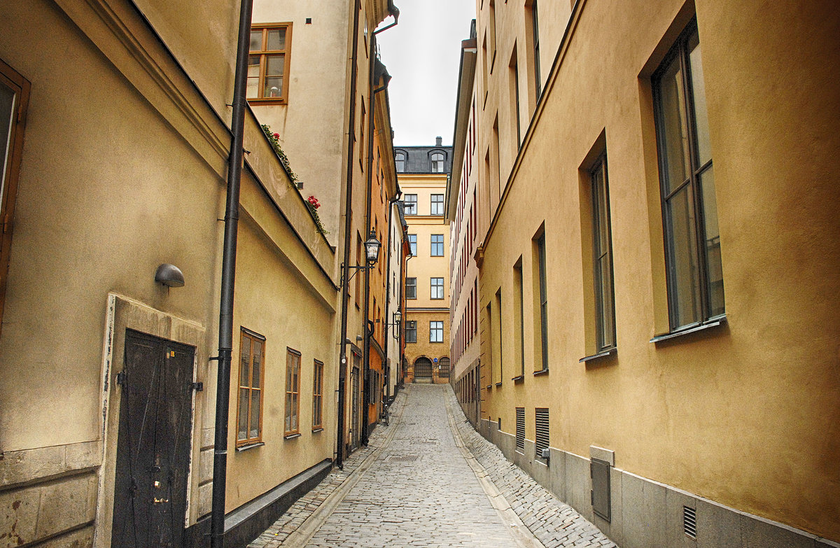 Gasse in der Stockholmer Altstadt (Gamla Stan).  In den Gebuden findet man hufig mittelalterliche Kellergewlbe, Kalkmalereien des 16. Jahrhunderts, reich verzierte Deckenbalken des 17. Jahrhunderts, hochklassige Innenausstattungen im Rokokostil oder berbordende Dekorationen des 19. Jahrhunderts.
Aufnahme: 25. Juli 2017.