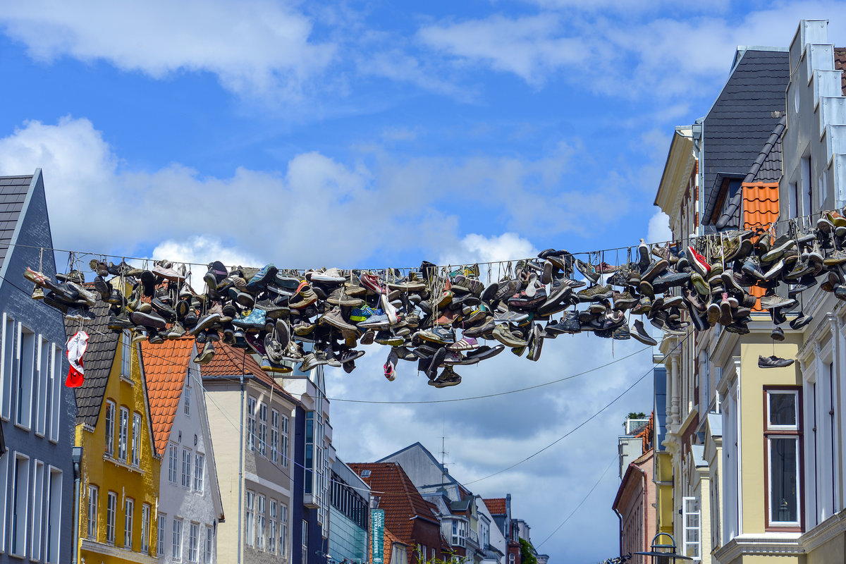 Hngende Schuhe in der Norderstrae in der Flensburger Innenstadt. In Flensburg, wo mehrere Leinen ber die Strae gespannt sind, wird das Phnomen beispielsweise schon ungefhr seit dem Jahr 2005 beobachtet. Hier soll das Phnomen dadurch entstanden sein, dass die Kunden eines Skatershops nach Kauf neuer Sneaker ihre alten Schuhe zurcklieen und der Ladenbesitzer sie ber die Leinen warf. Sein Nachbar vom St.-Pauli-Fanshop soll sich bald darauf angeschlossen haben. Die Schuhe der Norderstrae wurden zu einer Sehenswrdigkeit der Stadt und einem beliebten Fotomotiv. Aufnahme: 11. Juli 2020.