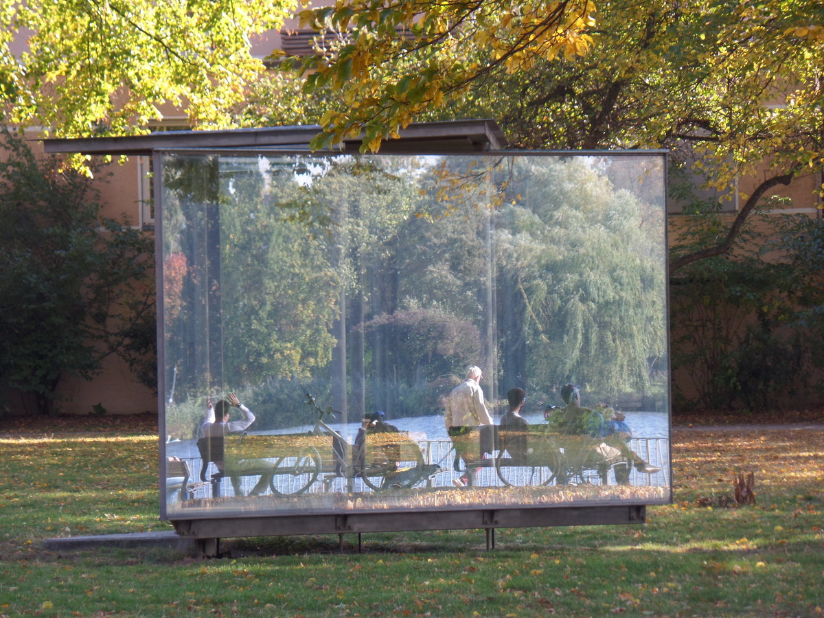 Hamburg am 11.10.2018: Spiegelungen im „Double Triangular Pavilion for Hamburg“ des Künstlers Dan Graham, in der Parkanlage „Uhlenhorster Fährhaus“ an der Außenalster, die zu sehenden Menschen sitzen am Alsterufer /