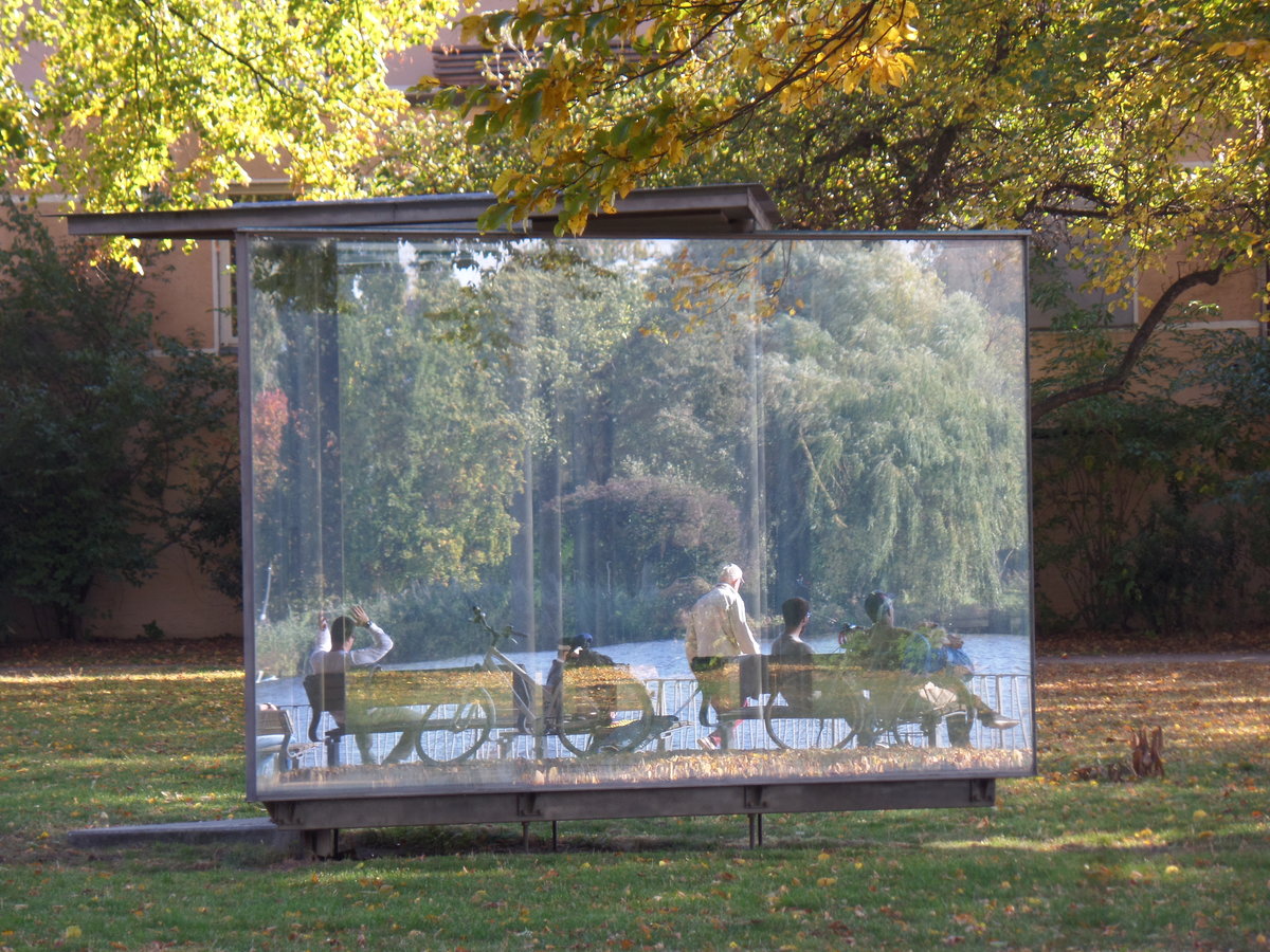 Hamburg am 11.10.2018: Spiegelungen im „Double Triangular Pavilion for Hamburg“ des Knstlers Dan Graham, in der Parkanlage „Uhlenhorster Fhrhaus“ an der Auenalster, die zu sehenden Menschen sitzen am Alsterufer /