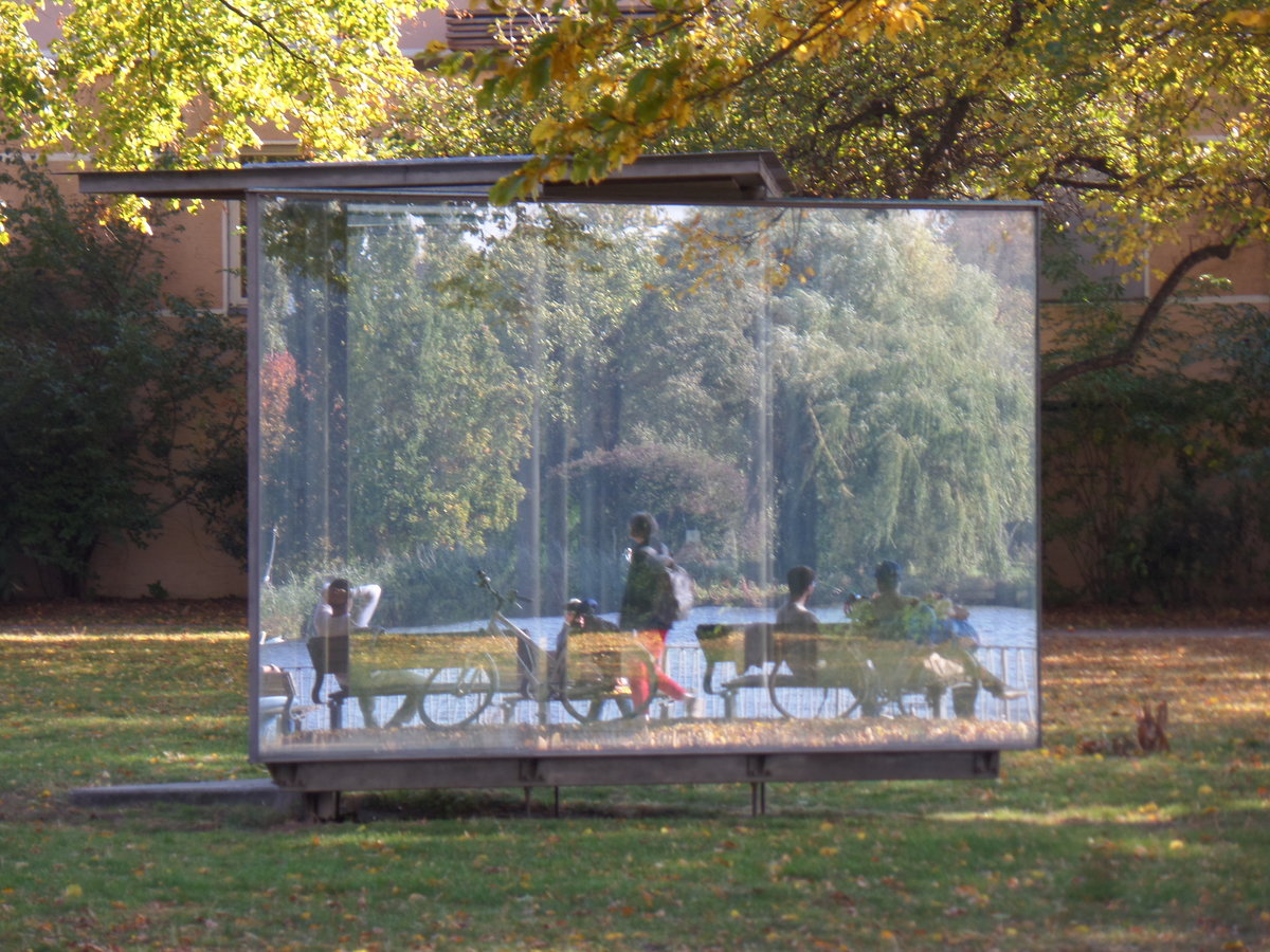 Hamburg am 11.10.2018: Spiegelungen im „Double Triangular Pavilion for Hamburg“ des Knstlers Dan Graham, in der Parkanlage „Uhlenhorster Fhrhaus“ an der Auenalster, die zu sehenden Menschen sitzen am Alsterufer /