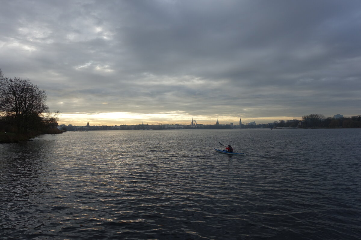 Hamburg am 11.12.2021: einsamer Paddler auf der Auenalster vor der Stadtkulisse /