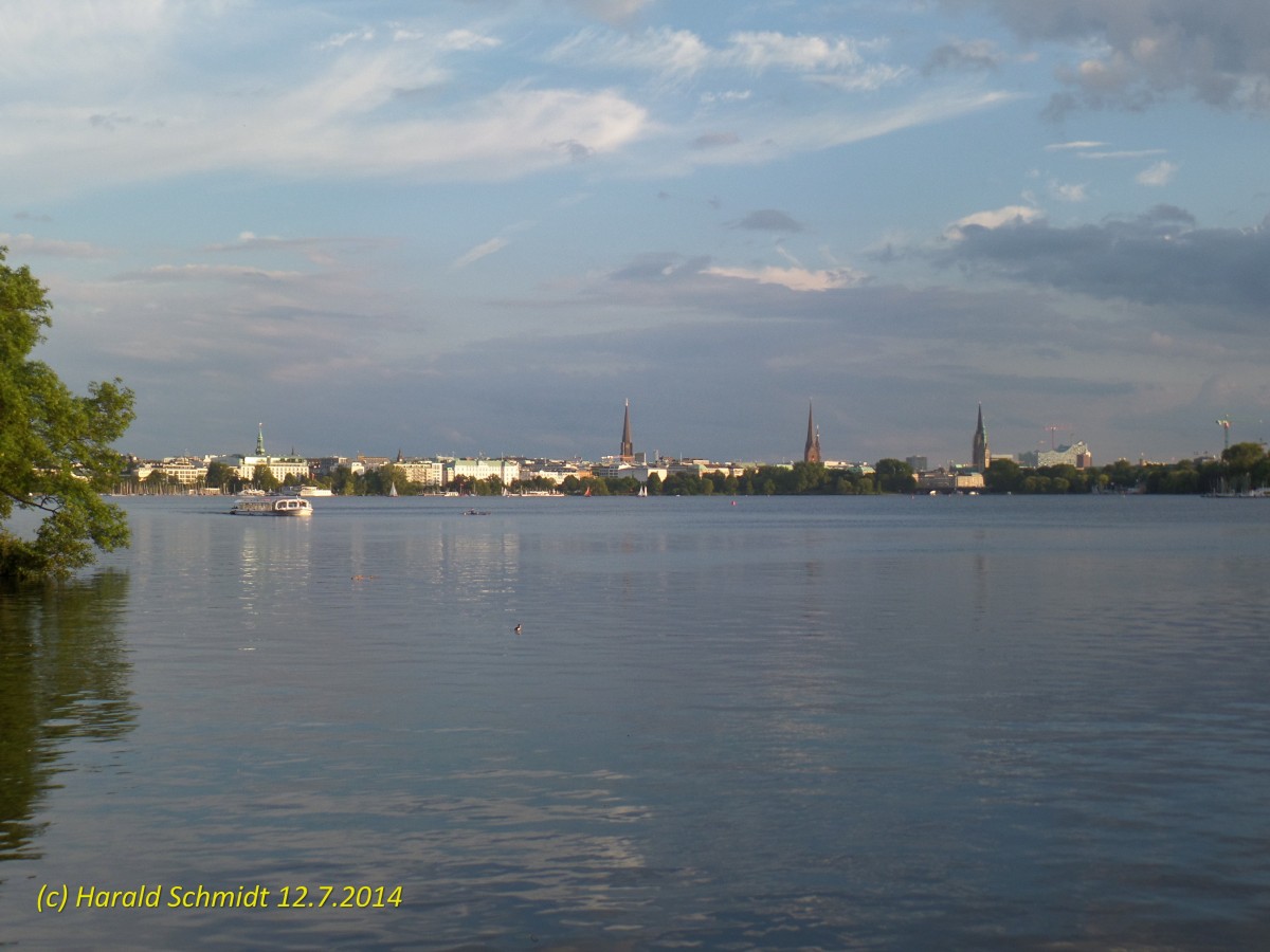 Hamburg am 12.7.2014: Blick ber die Auenalster nach St. Georg und zur Innenstadt. Die Trme sind von links nach rechts: St. Georg-Kirche, St. Jakobi-Kirche, St.  Petri-Kirche, verdeckt St. Katharinen-Kirche, Rathaus, dahinter unter Gerst die St. Nikolai-Kirche